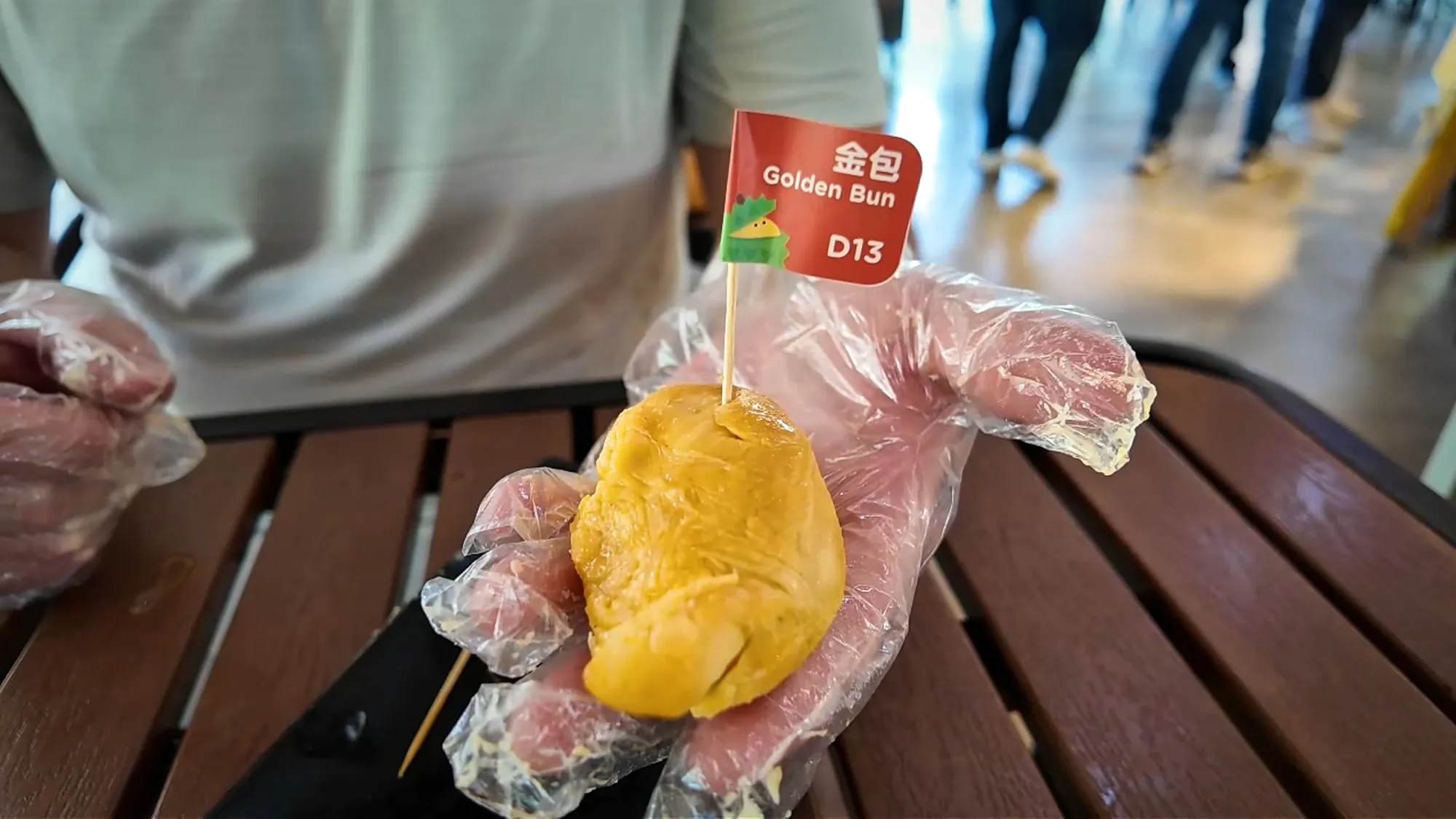 A gloved hand holding a bright orange-yellow Golden Bun durian piece with a red flag marked D13.