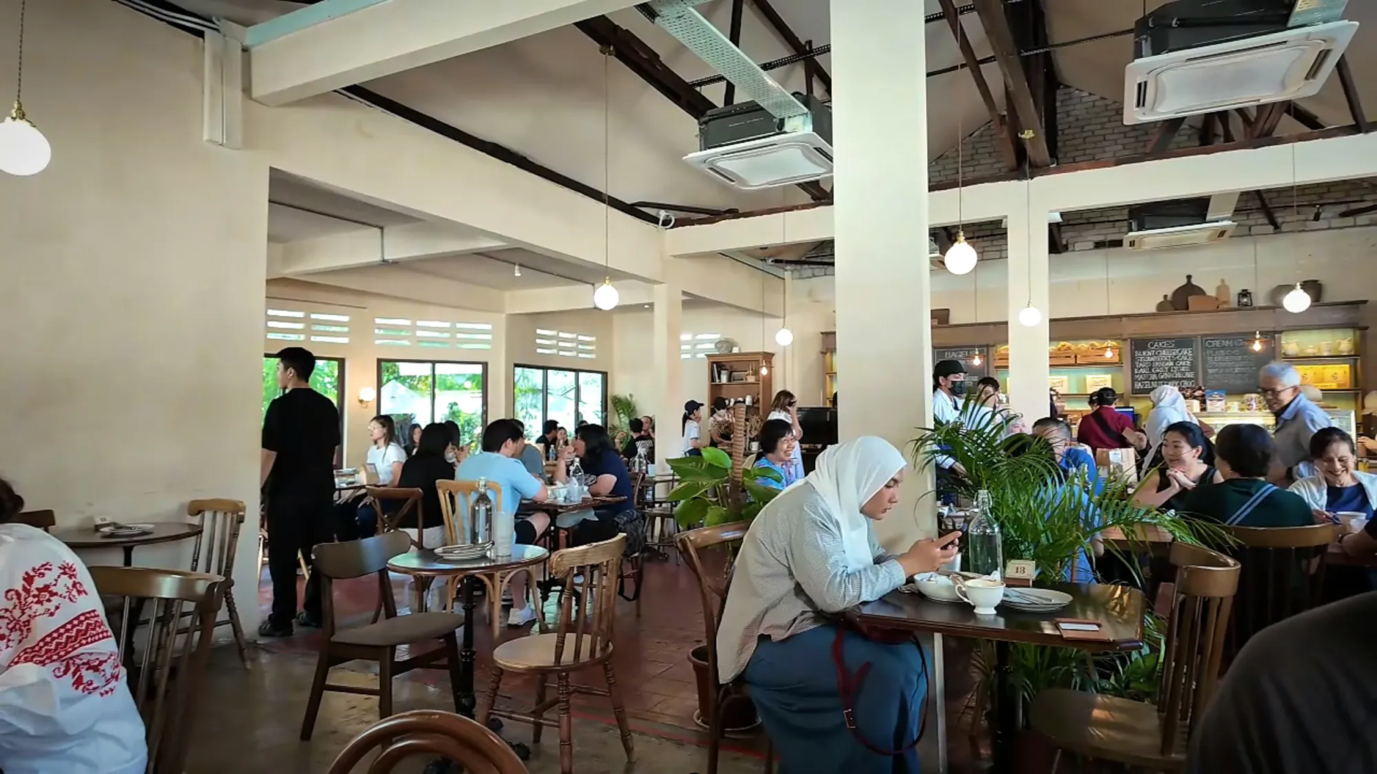 Busy dining room at Grumpy Bagels with wooden tables, ceiling fans, pendant lights, and tall windows letting in daylight.