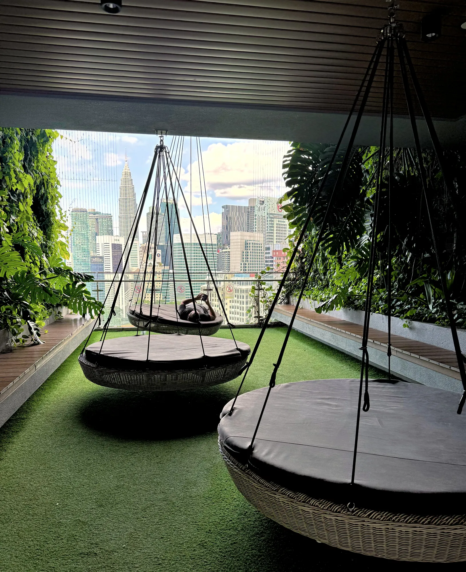 Round woven hanging chairs on the rooftop garden at Ceylonz Suites, looking out at the Kuala Lumpur skyline.