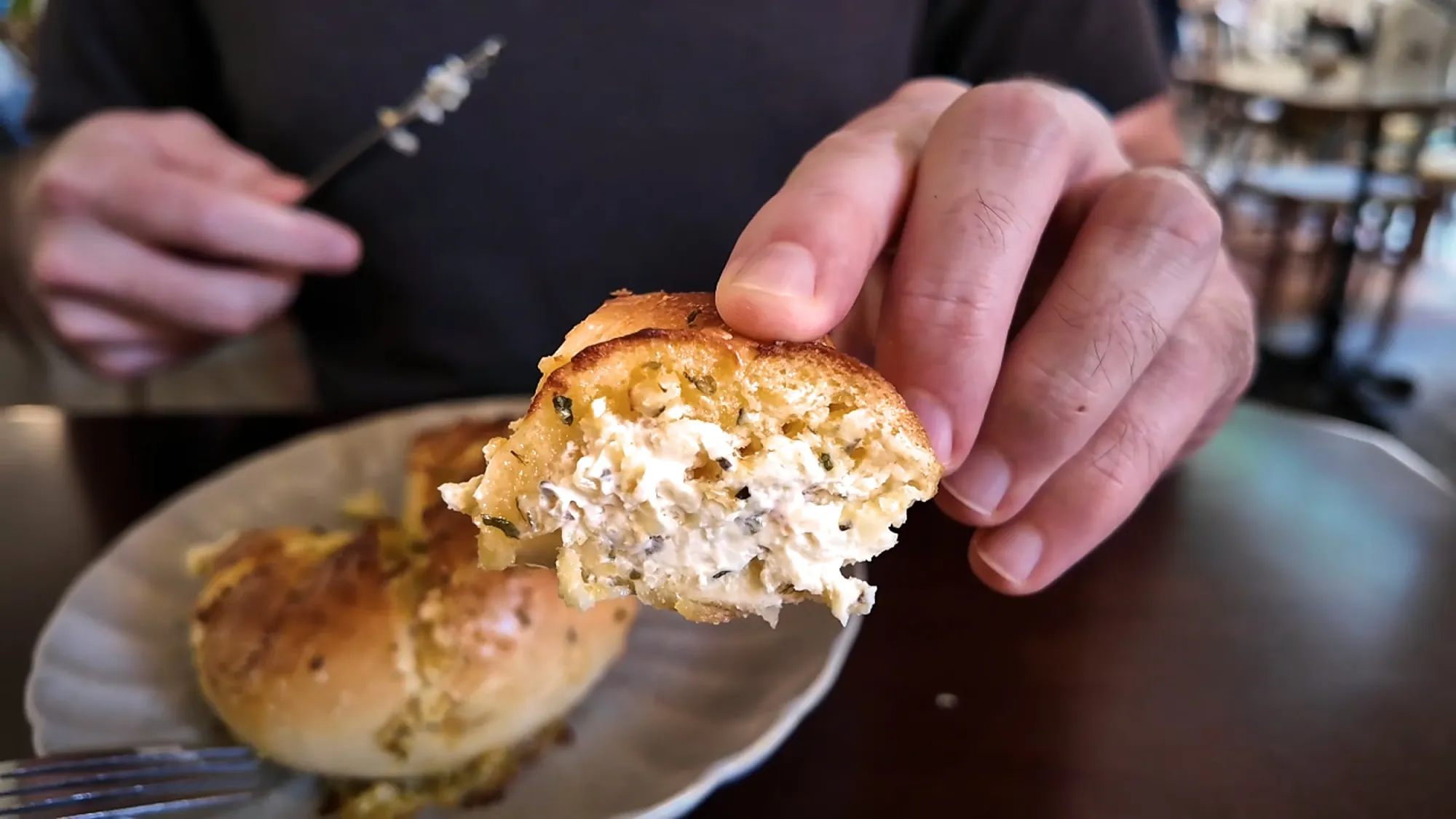 Hand holding a torn piece of the garlic bagel to show the cream cheese filling inside.