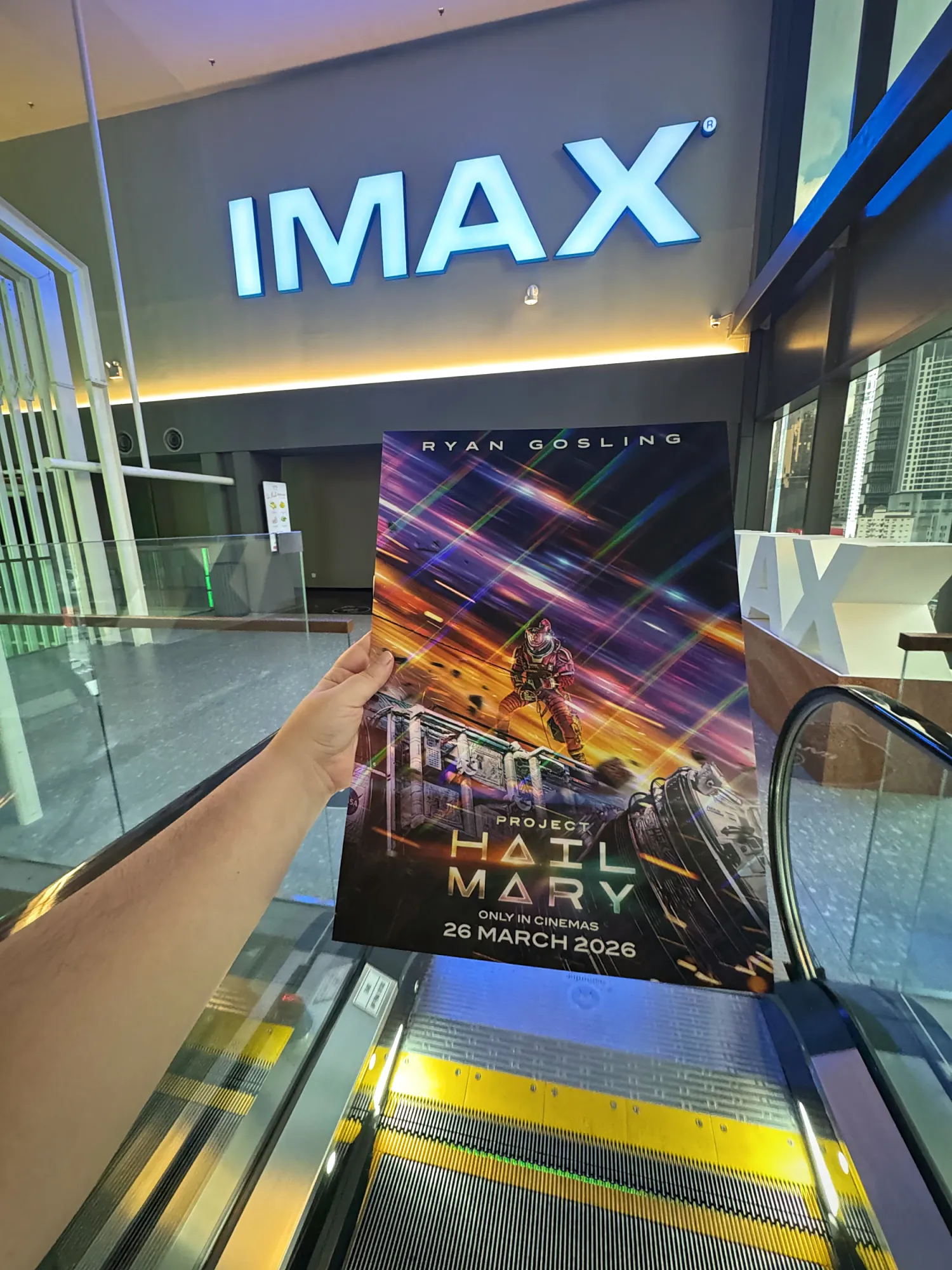A hand holding a Project Hail Mary movie poster in front of the lit IMAX sign at Aurum Theatre, The Exchange TRX, Kuala Lumpur.