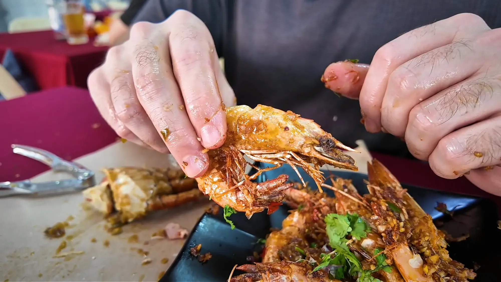 Peeling a crispy fried prawn over a plate of prawns at Restoran Fatty Crab, Petaling Jaya.