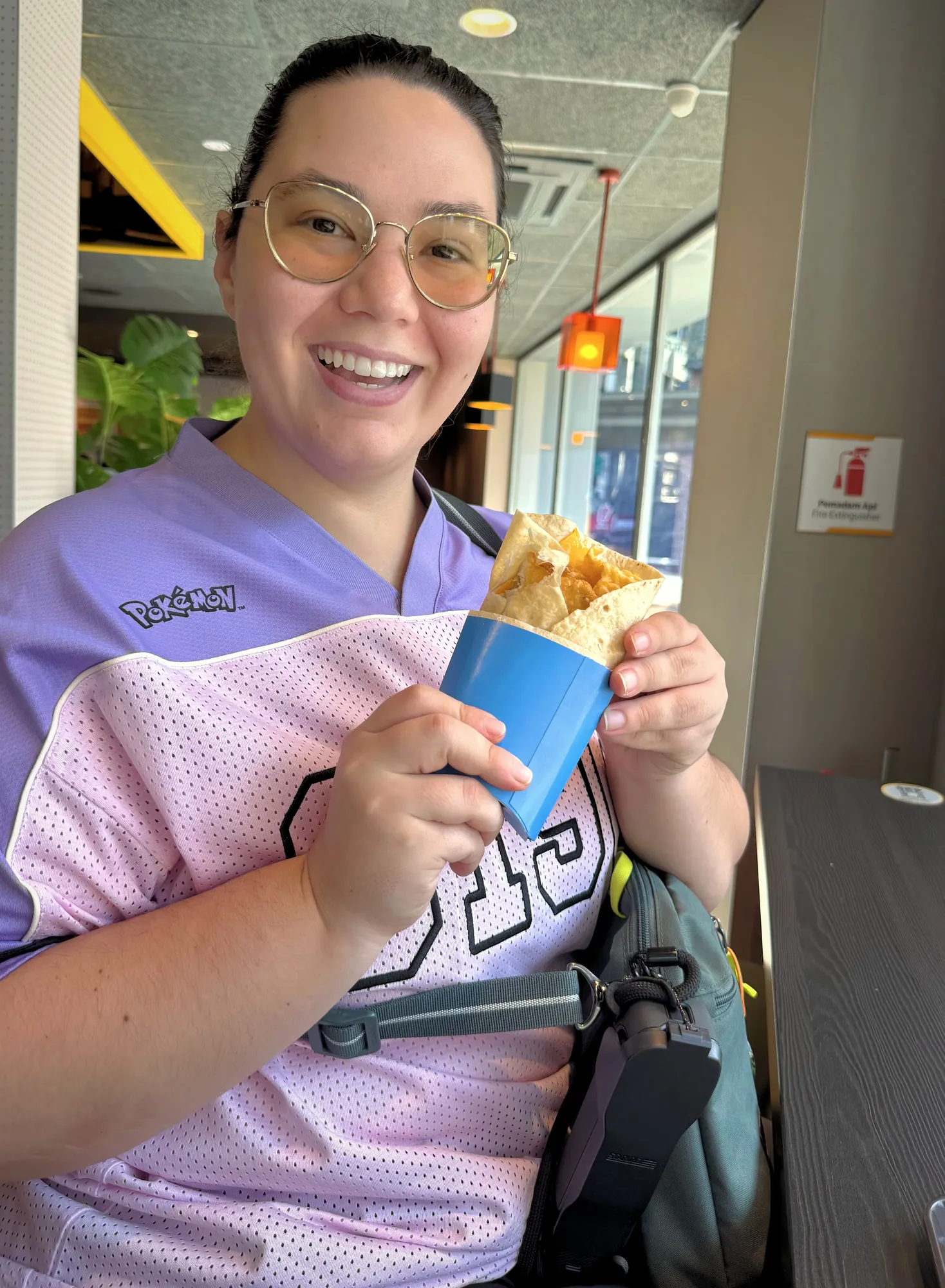 A joyful woman wearing glasses holds a McDonald's breakfast wrap inside the Bukit Bintang McDonald's dining area.