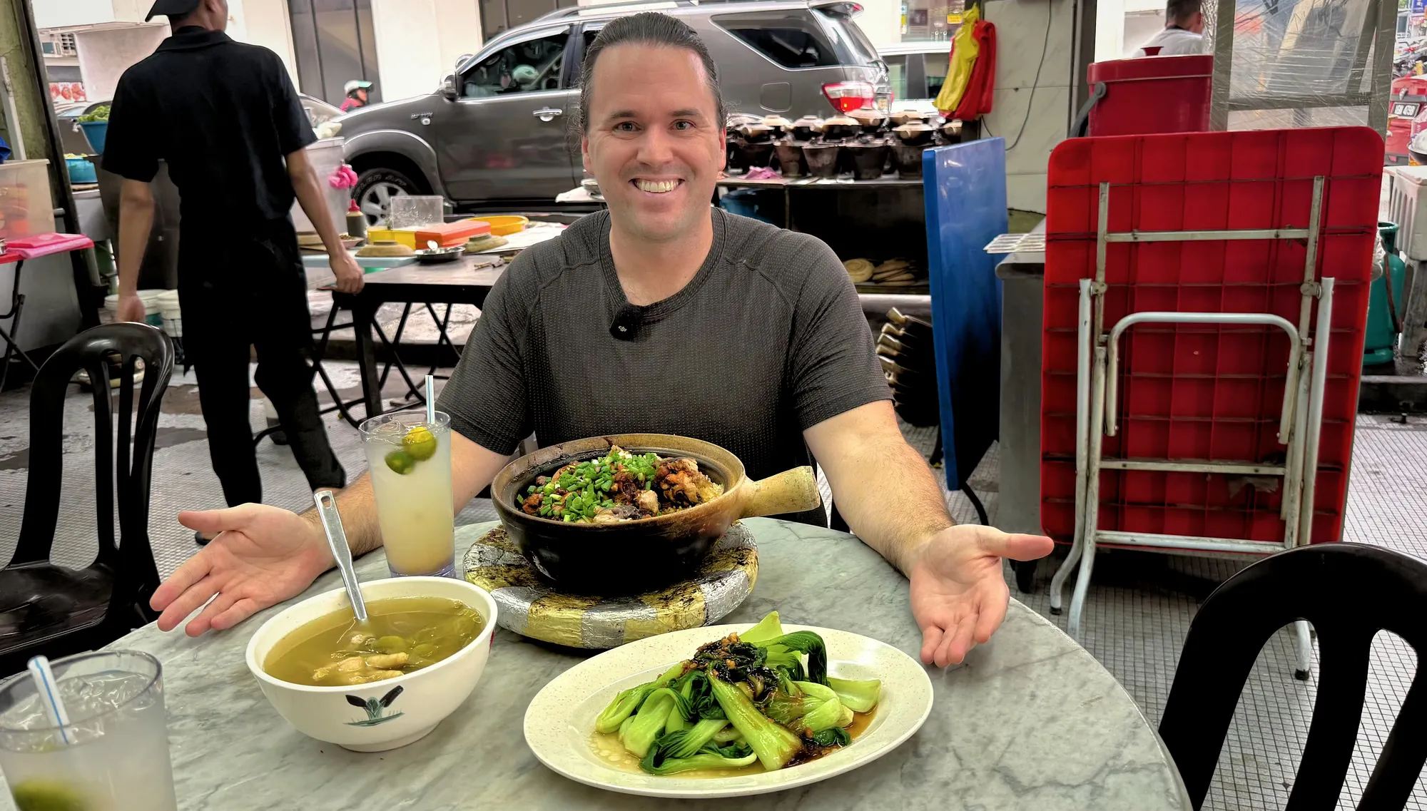 Gesturing at a street-side table with claypot chicken rice and greens at 168 Claypot Chicken Rice in Kuala Lumpur