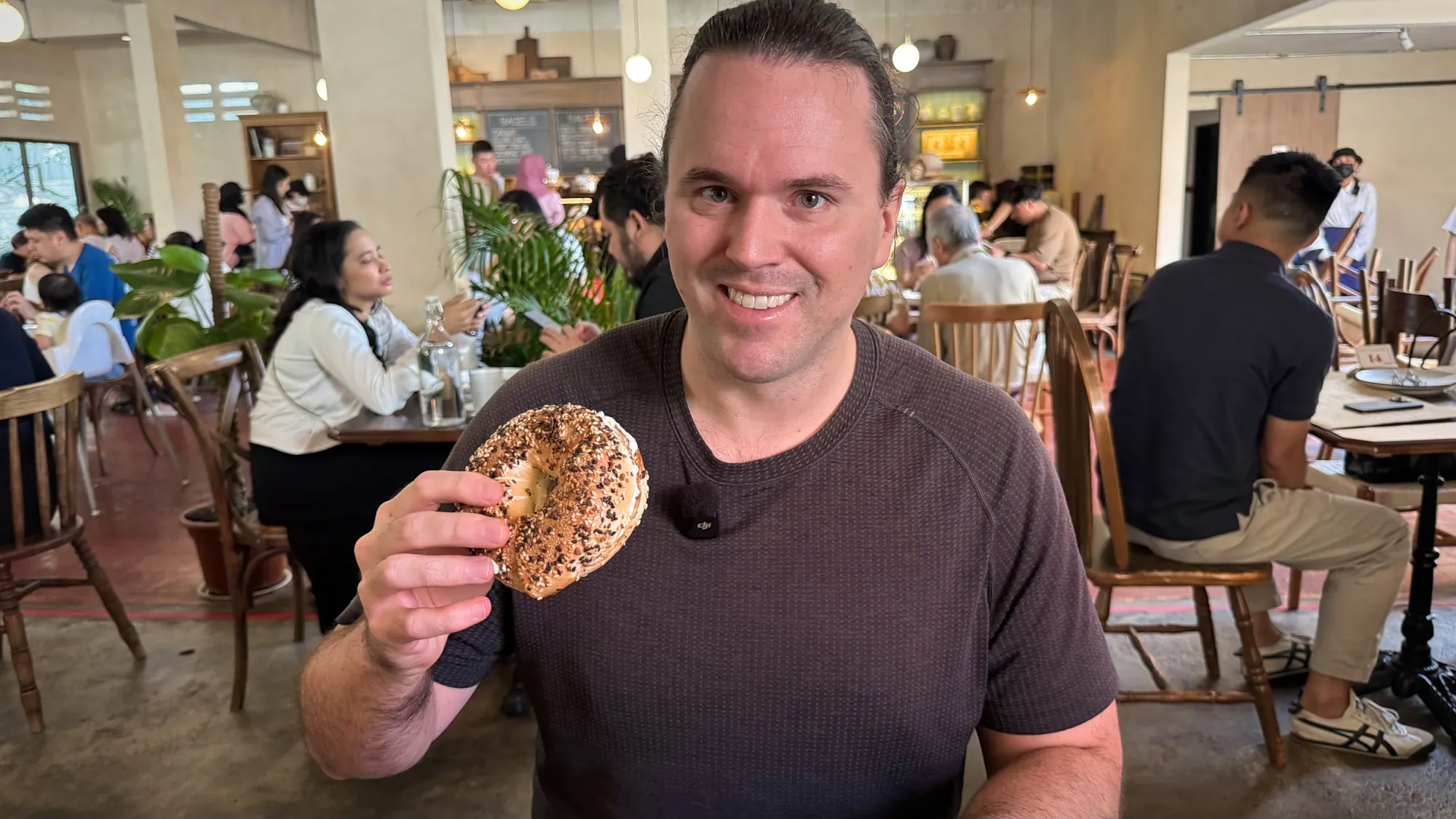 Cream holding up a bitten everything bagel in the busy Grumpy Bagels dining room in Kuala Lumpur.