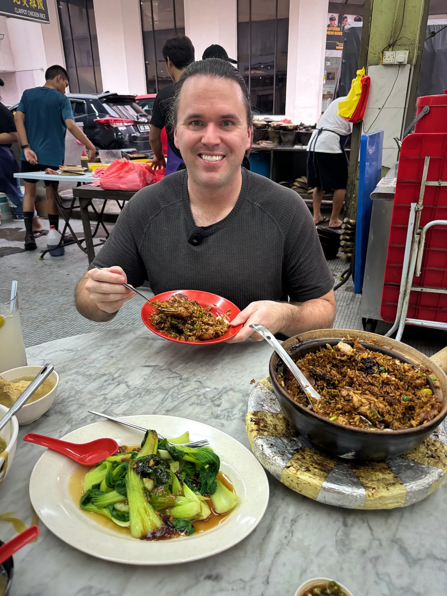 Cream smiling and holding a plate of claypot chicken rice at the open-air 168 coffee shop in Pudu, Kuala Lumpur.