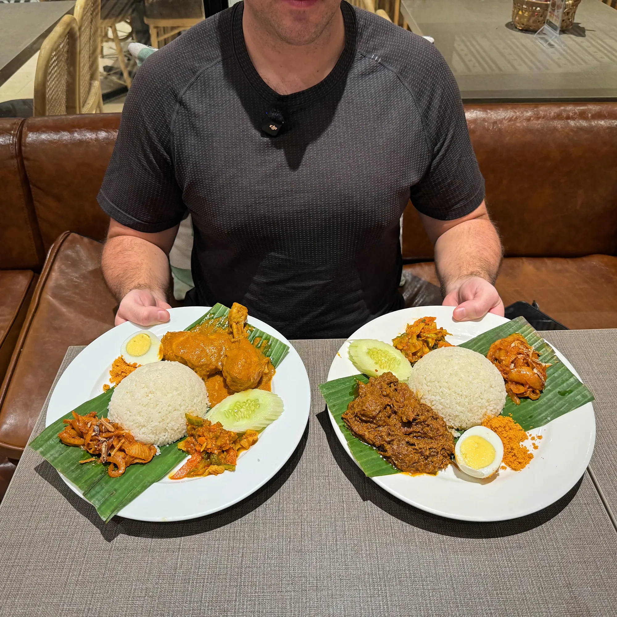 Cream holding two plates of nasi lemak on banana leaves, one with curry chicken and one with beef rendang, at Madam Kwan's in Pavilion Kuala Lumpur.