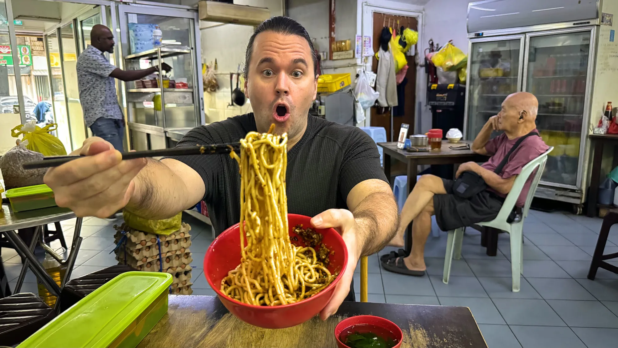 Cream looking amazed as he lifts noodles from a bowl of chili pan mee inside Restoran Kin Kin.
