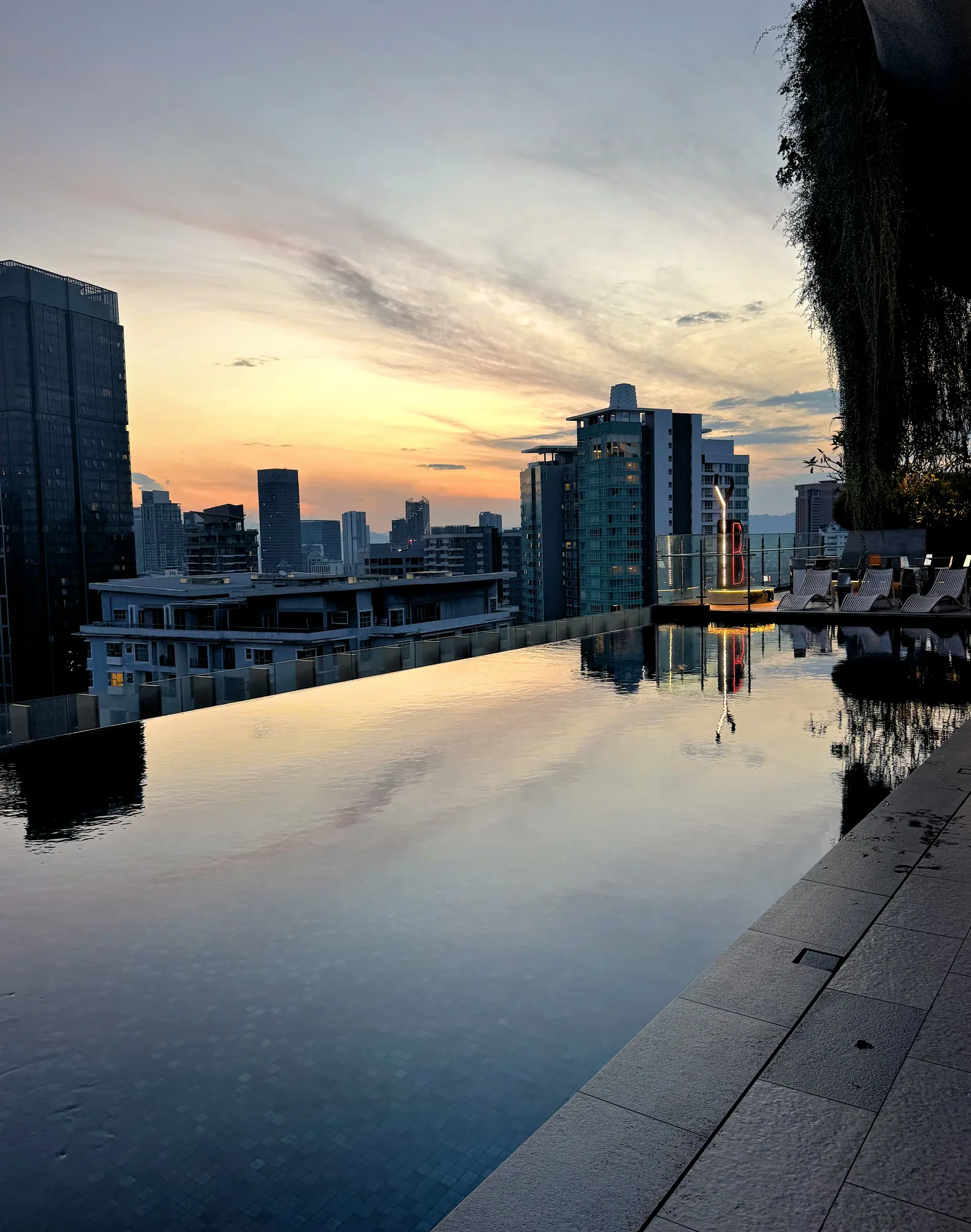 Golden sunrise light reflecting across a rooftop infinity pool overlooking modern high-rises in Kuala Lumpur.