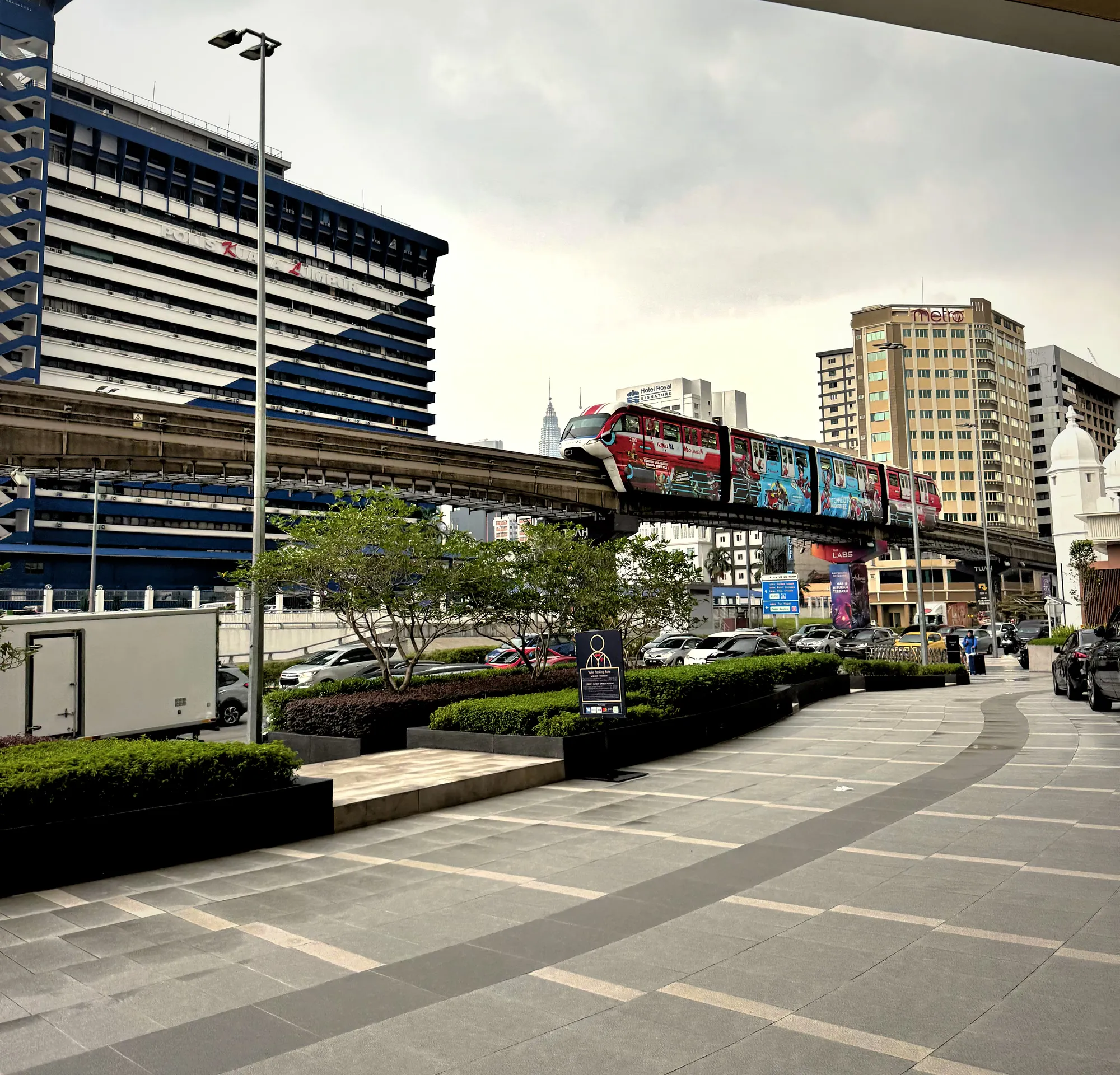 A red KL Monorail train on its elevated track past office towers in Bukit Bintang, Kuala Lumpur.