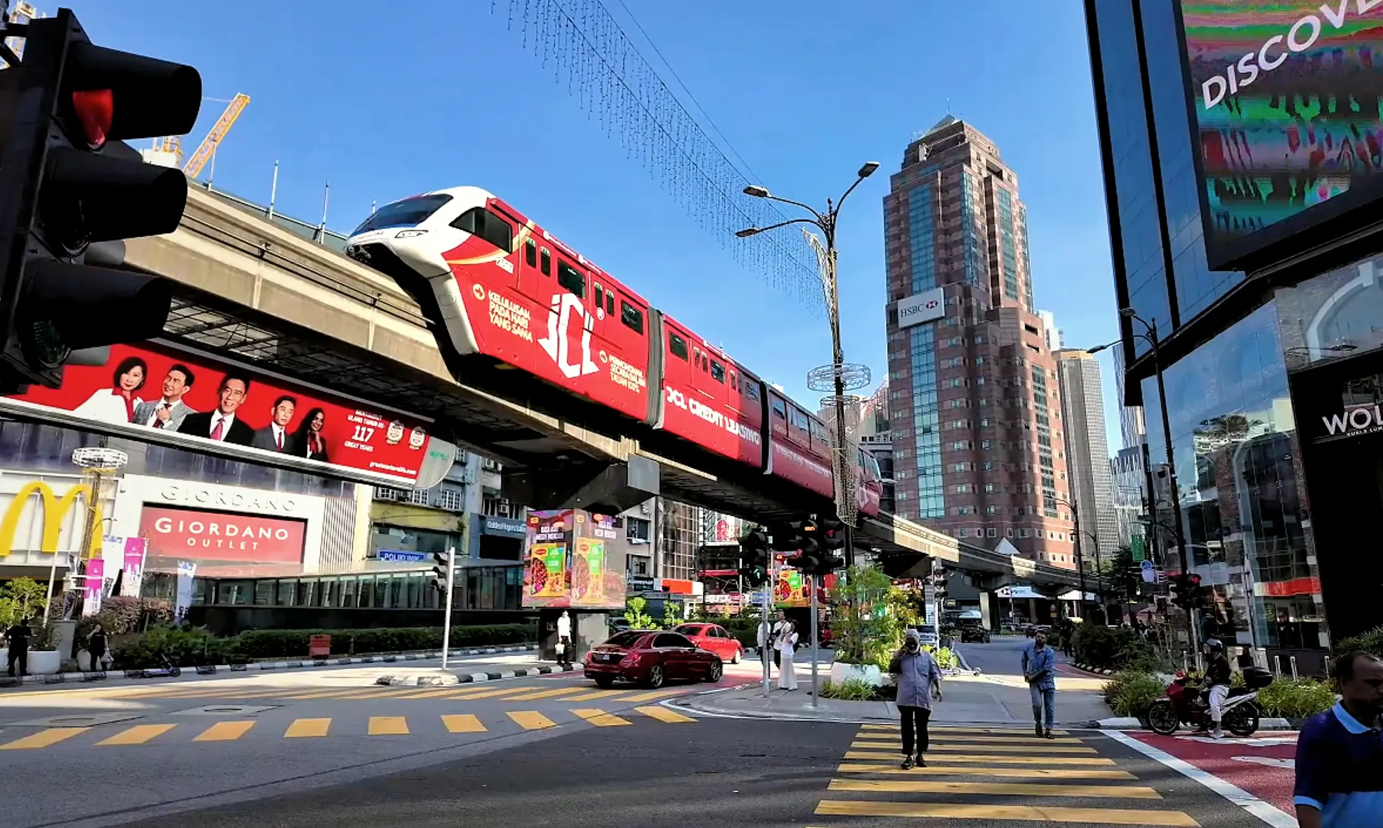 A red KL Monorail train on its elevated track above the busy Bukit Bintang intersection in Kuala Lumpur.
