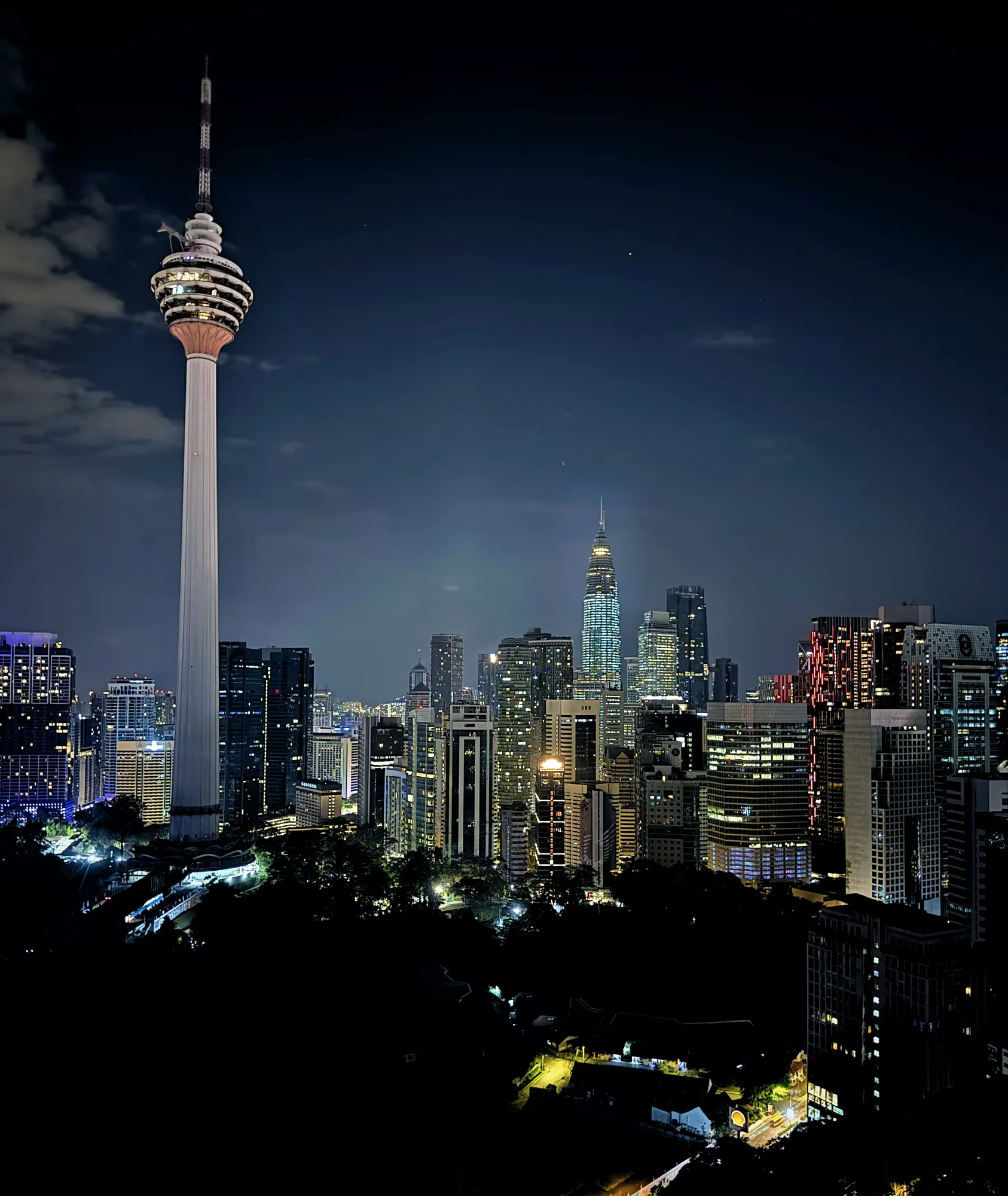 Menara Kuala Lumpur and the Petronas Twin Towers lit up in the Kuala Lumpur skyline at night.