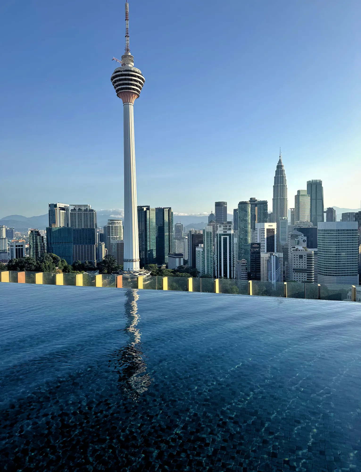 The spire of KL Tower reflected across the rippling blue water of the rooftop infinity pool at Ceylonz Suites, Kuala Lumpur.