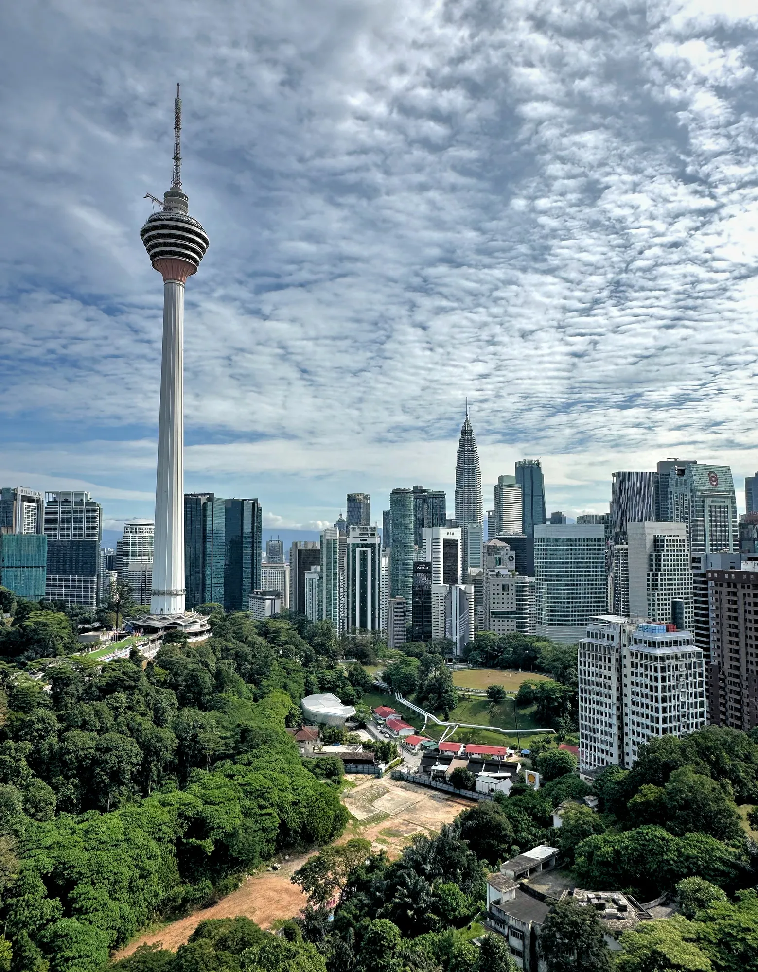 Panoramic daytime view of the KL Tower and Kuala Lumpur city skyline surrounded by lush green parks.