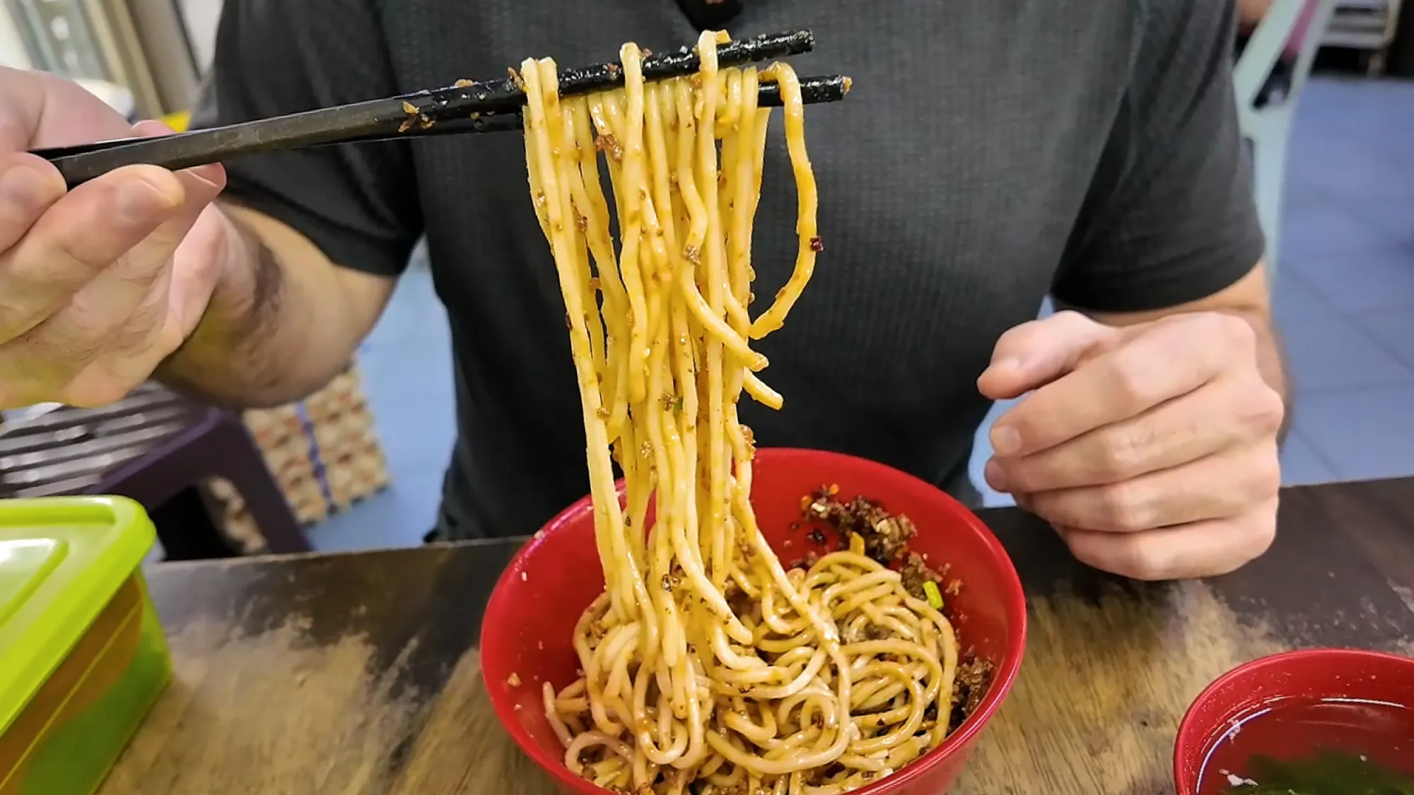 Cream lifting a chopstick-full of mixed dry chili pan mee coated in egg and minced pork at Kin Kin.