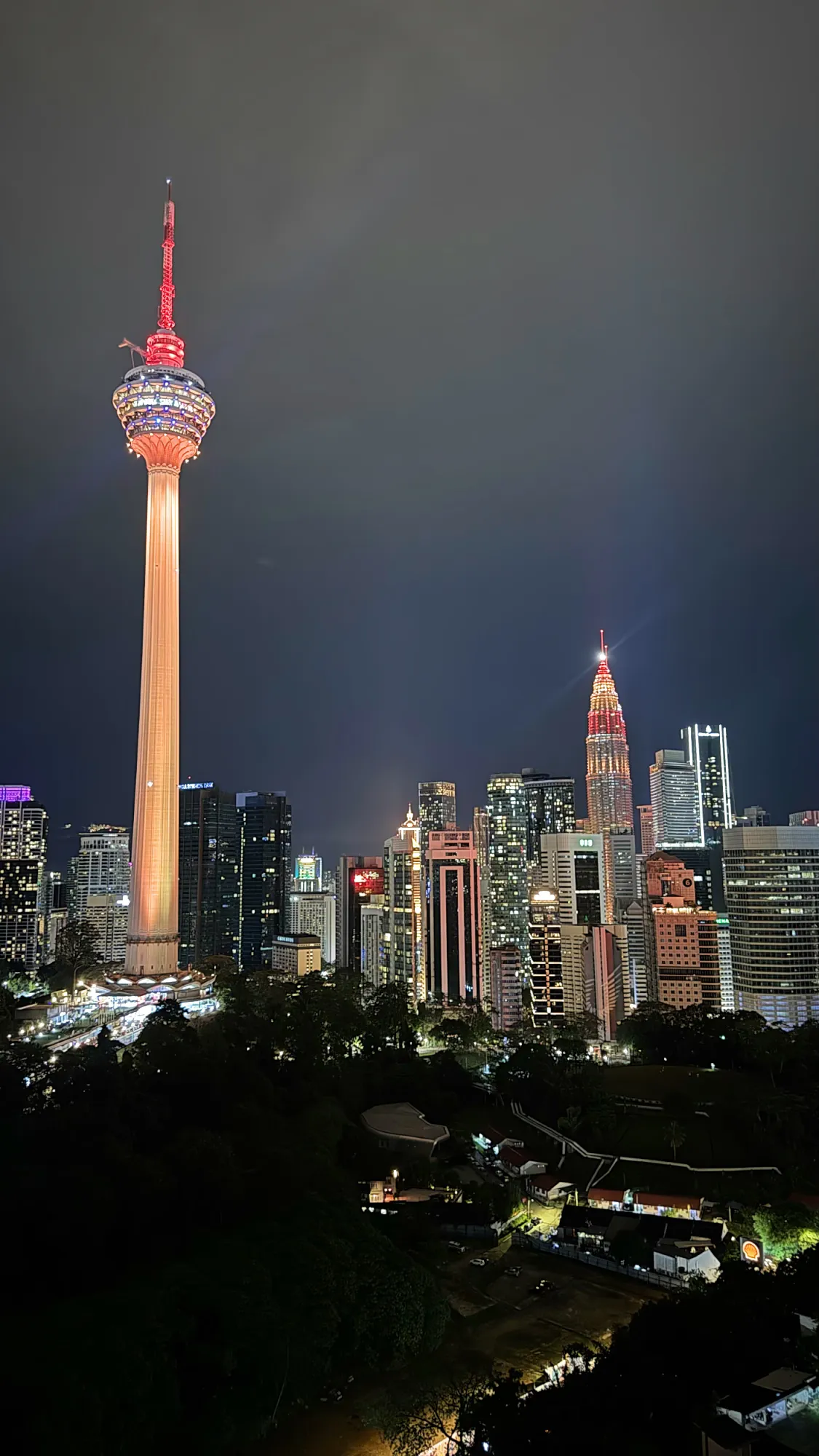 The KL Tower with a red-lit top and the Petronas Twin Towers glowing red and gold over the Kuala Lumpur skyline at night during Chinese New Year.