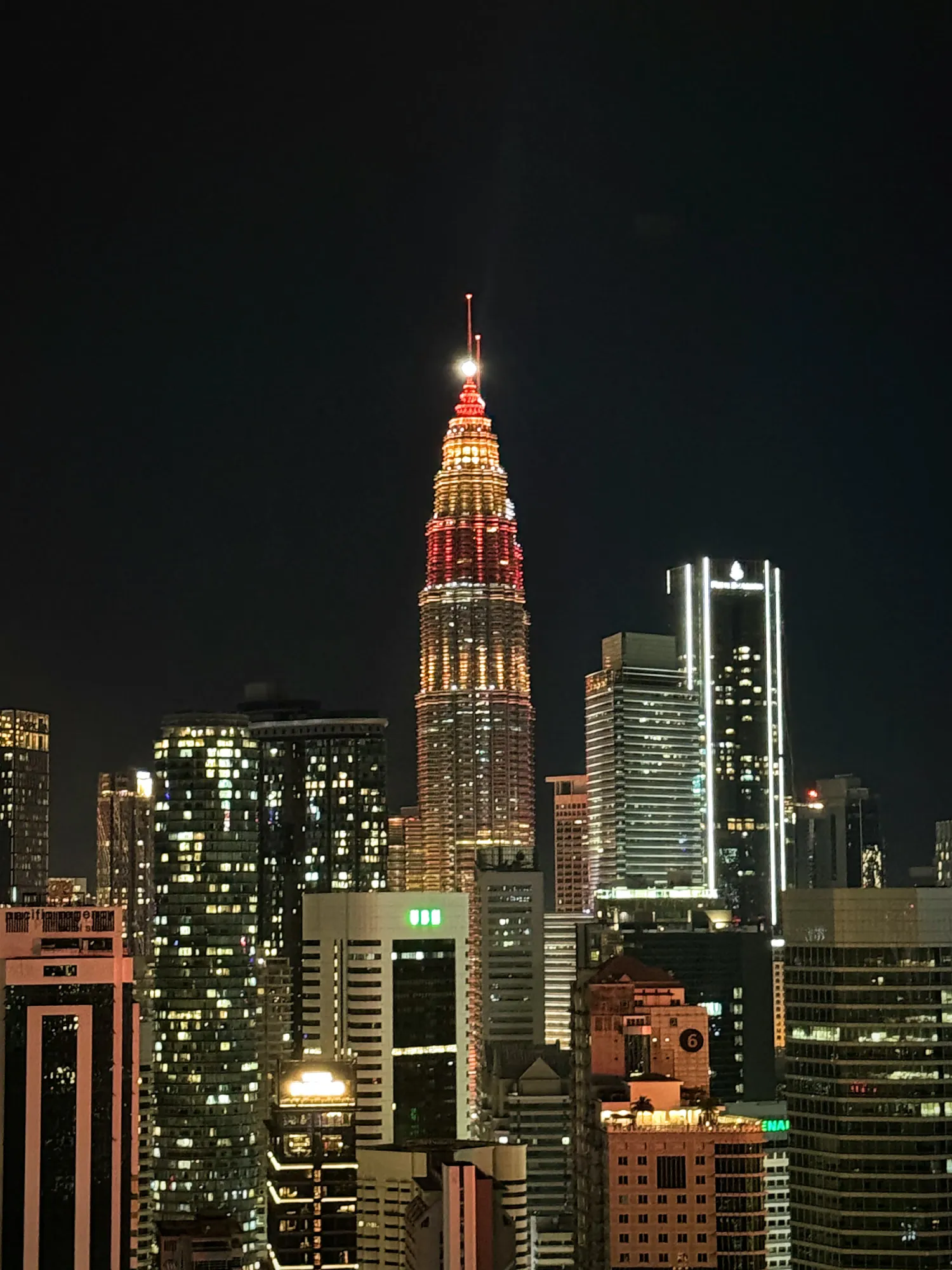 A Petronas Twin Tower lit in red and gold at night for Chinese New Year above the high-rises of Kuala Lumpur.