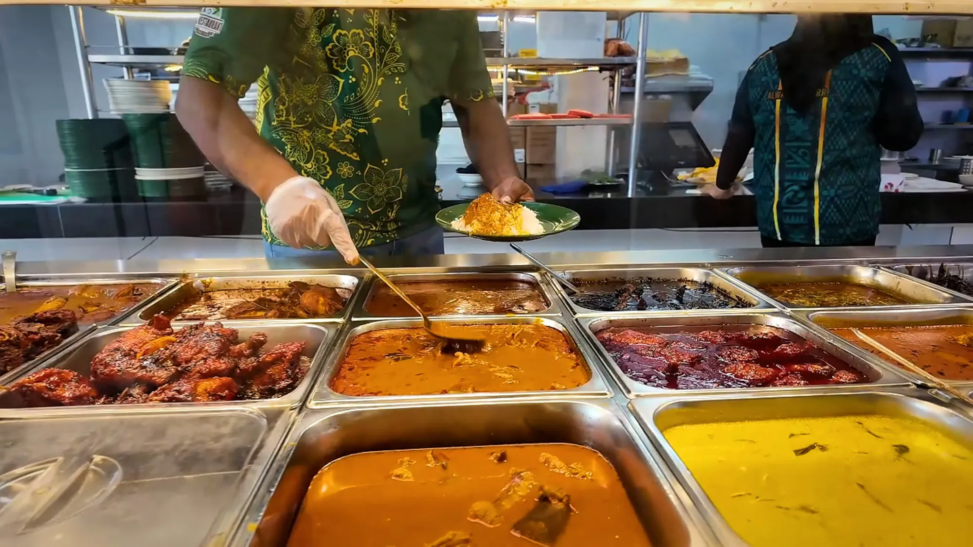 A server plating rice behind trays of curries and fried chicken at the Line Clear nasi kandar counter in Kampung Baru, Kuala Lumpur.