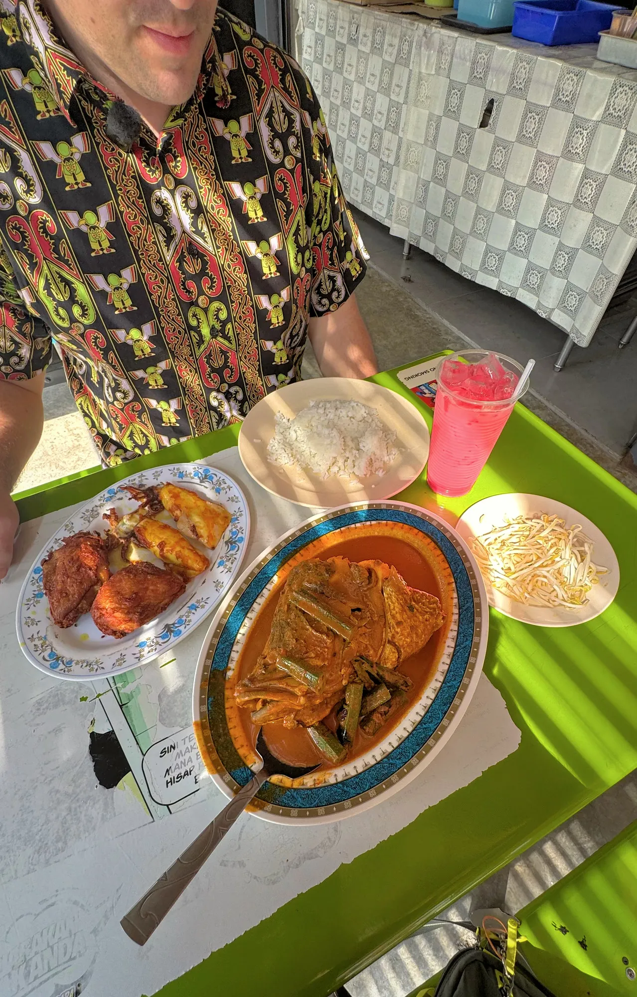 Sitting at a green table filled with fish head curry, fried chicken, rice, beansprouts, and sirap bandung at Anuar's in Kuala Lumpur