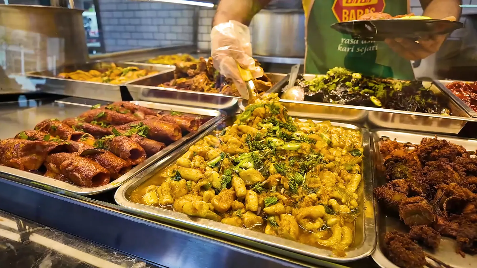 A closer look at the trays of stuffed squid, squid, and fried chicken as a server builds a plate behind the counter at Saddam Nasi Kandar in Kuala Lumpur.