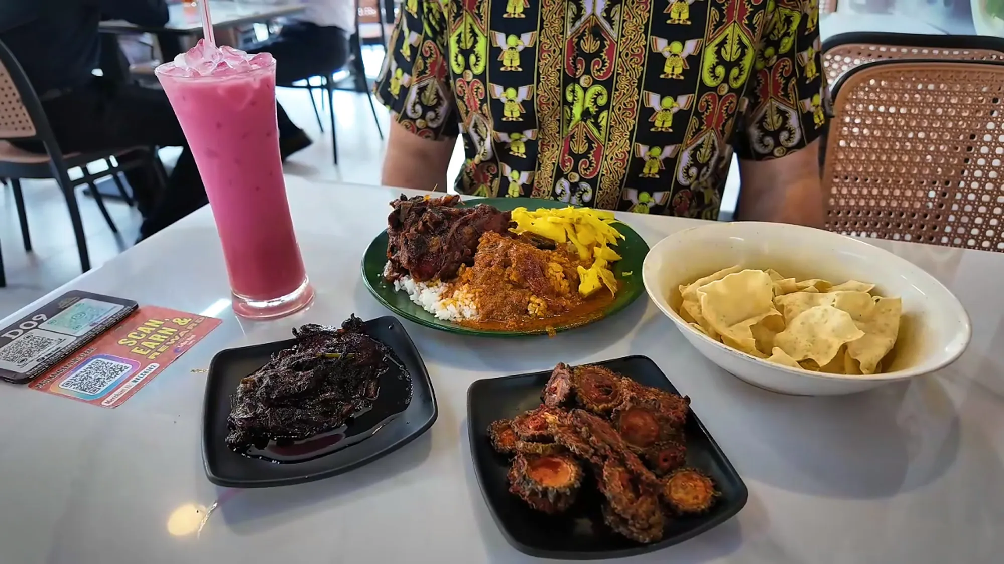 Our table at Line Clear in Kampung Baru, Kuala Lumpur, with nasi kandar on a green plate, fried bitter gourd, a bowl of papadum, and a tall pink sirap bandung.