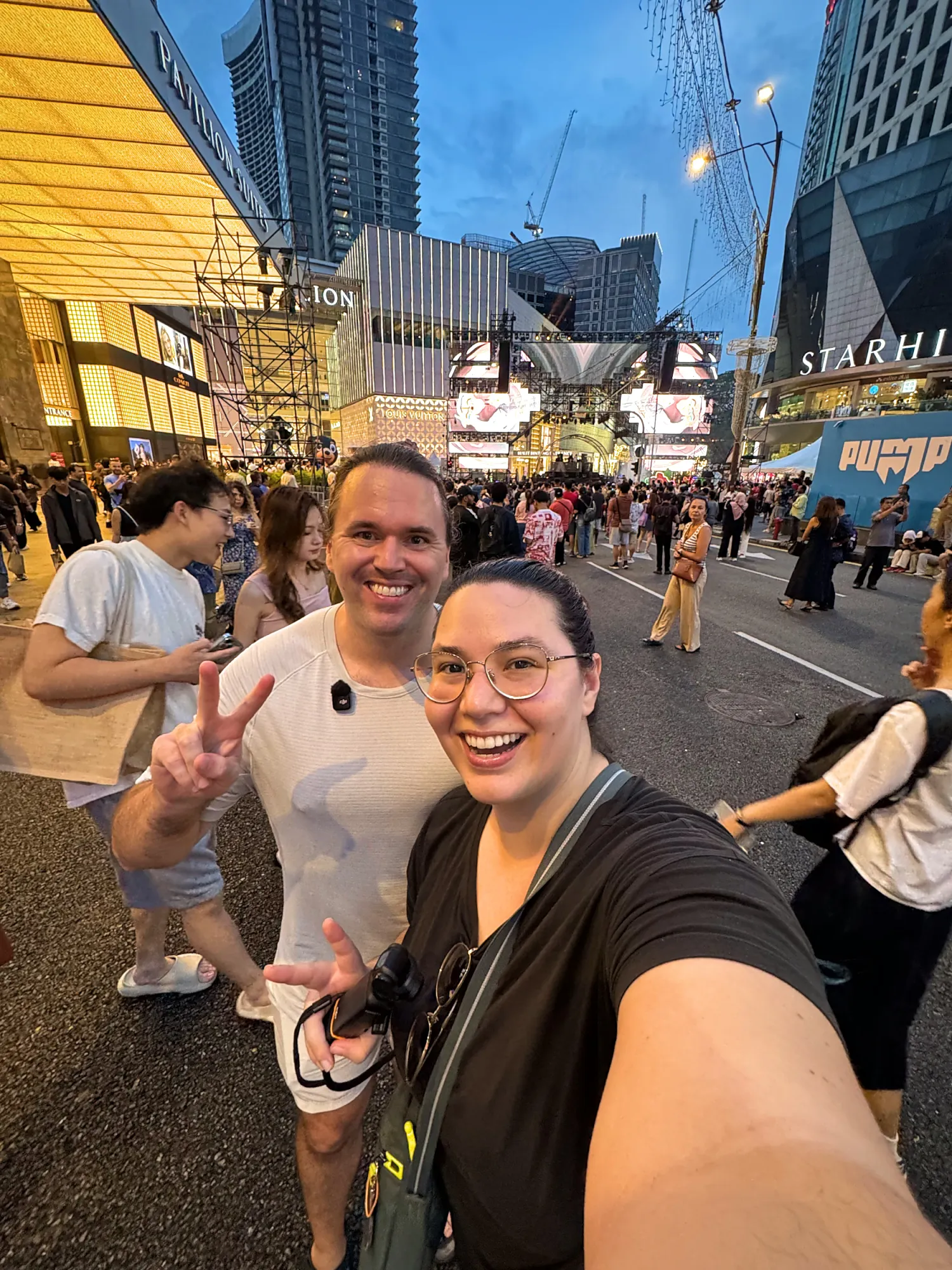 Bernie and Cream taking a selfie on a crowded Jalan Bukit Bintang in the evening, with The Starhill and the shopping strip behind them.