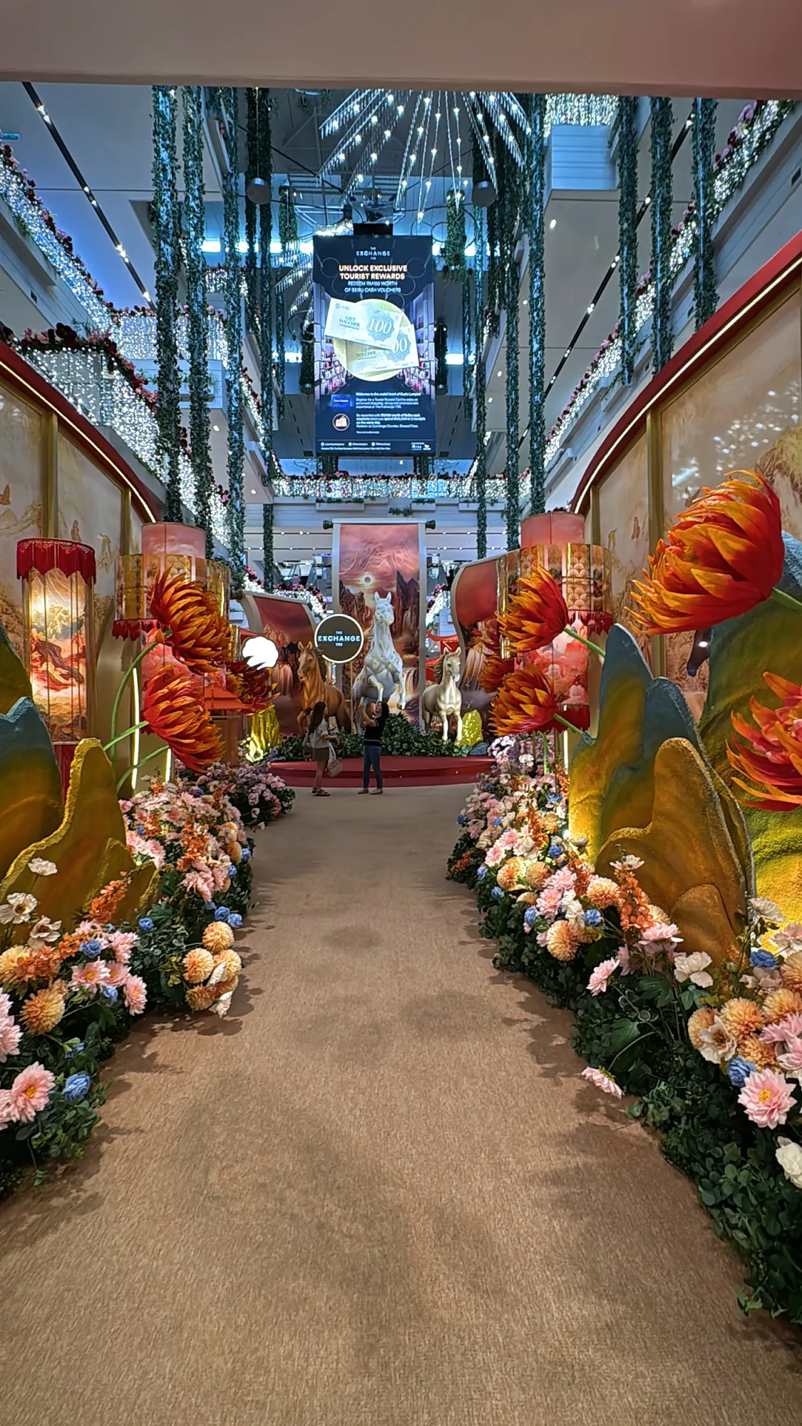 A carpeted walkway lined with giant artificial flowers and floral arches leading to a Lunar New Year horse display at The Exchange TRX in Kuala Lumpur.