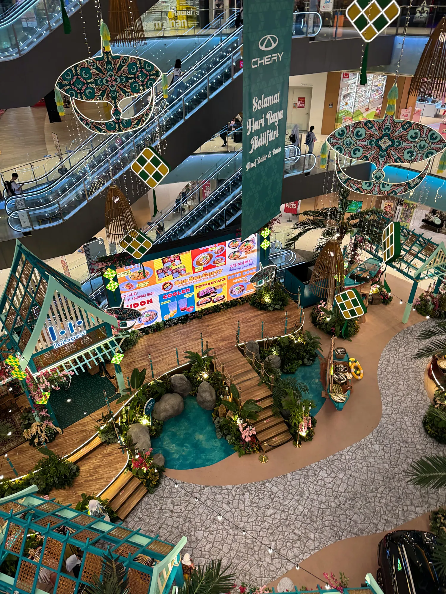 Looking down on a Hari Raya display with a garden, pond, and decorations in the atrium of LaLaport BBCC in Kuala Lumpur.
