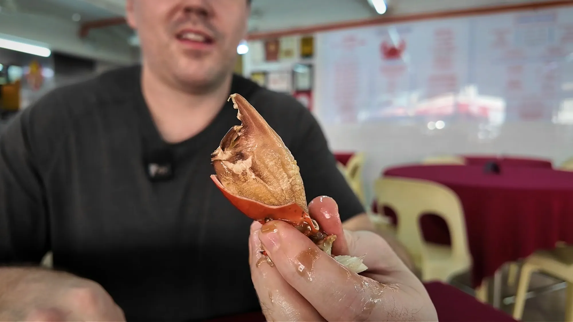 Cream holding up a large cracked crab claw coated in chilli sauce inside Restoran Fatty Crab.