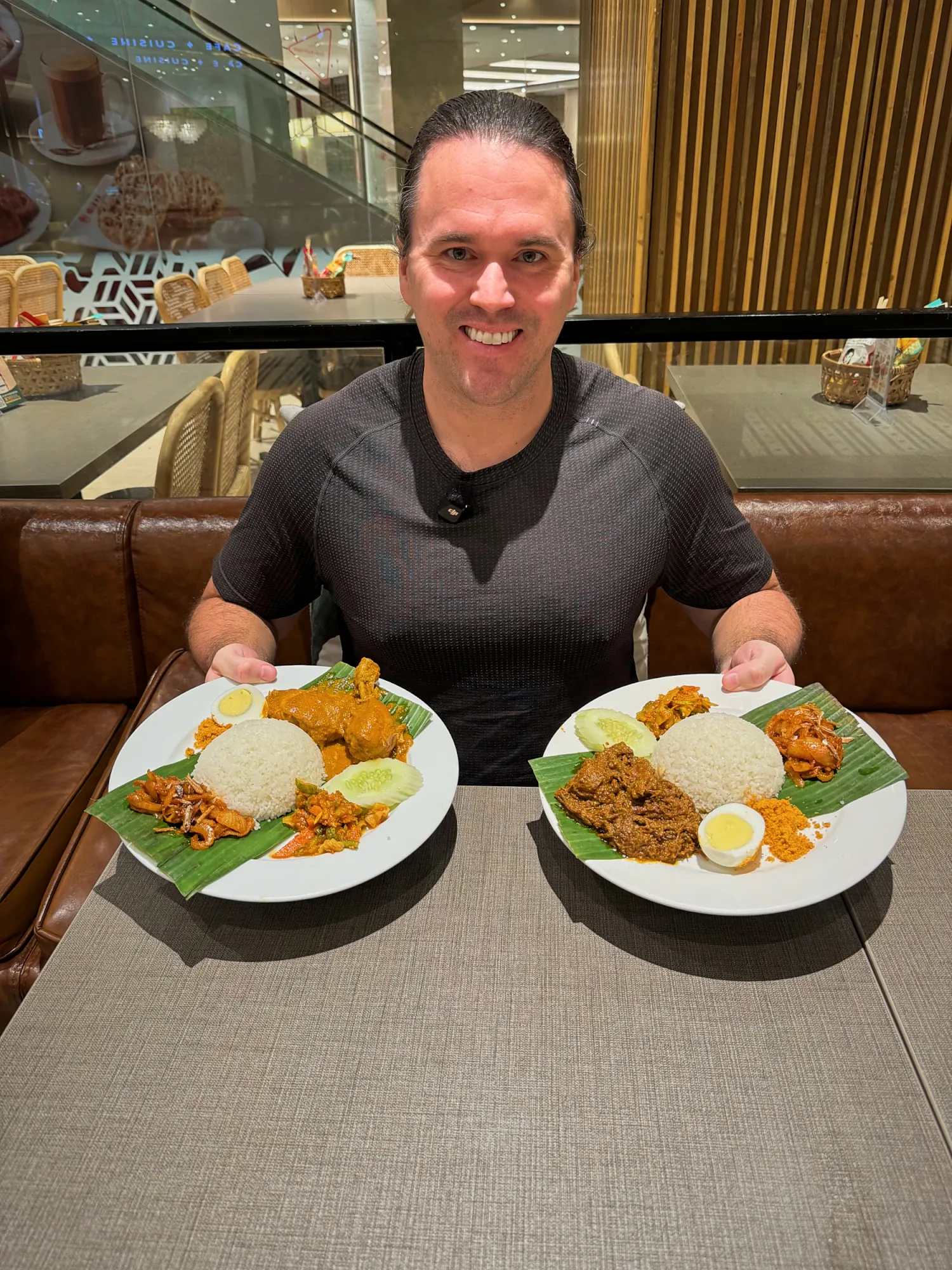 Cream smiling with two plates of nasi lemak on banana leaves at a table in Madam Kwan's, Pavilion Kuala Lumpur.