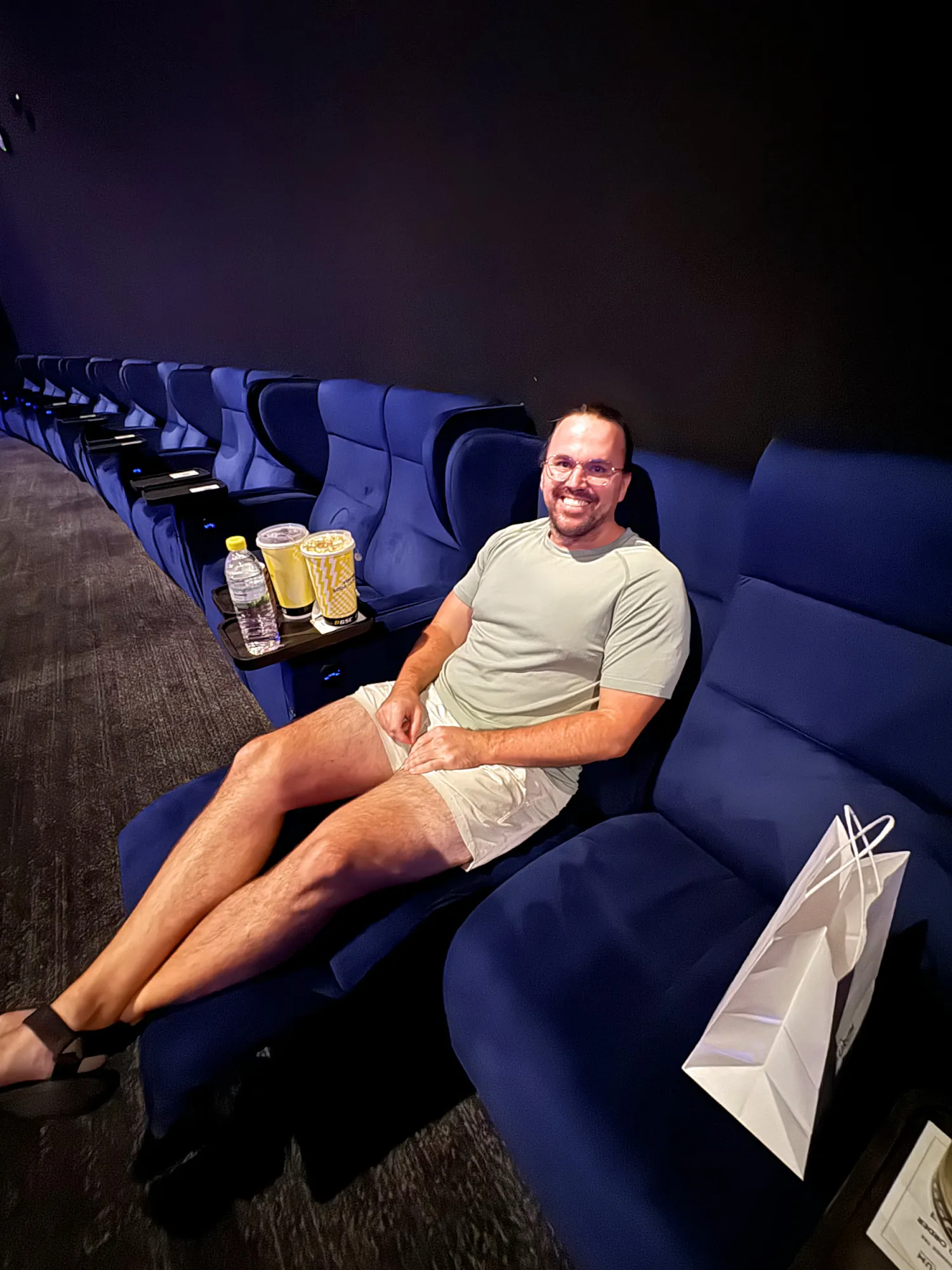 Cream smiling in a blue velvet IMAX recliner with popcorn and drinks beside him at Aurum Theatre, Kuala Lumpur.
