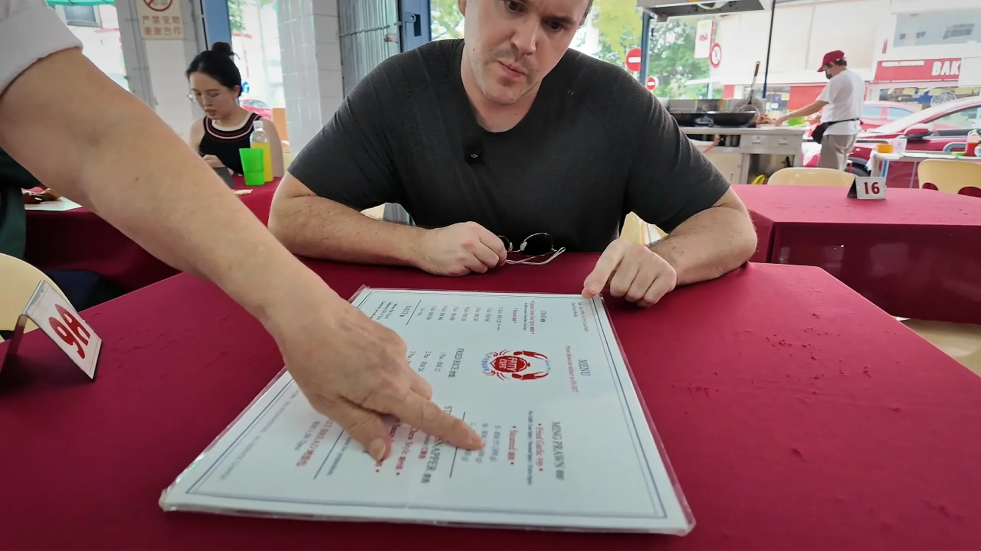 A server pointing out dishes on the menu for Cream at a red-clothed table inside Restoran Fatty Crab, Petaling Jaya.