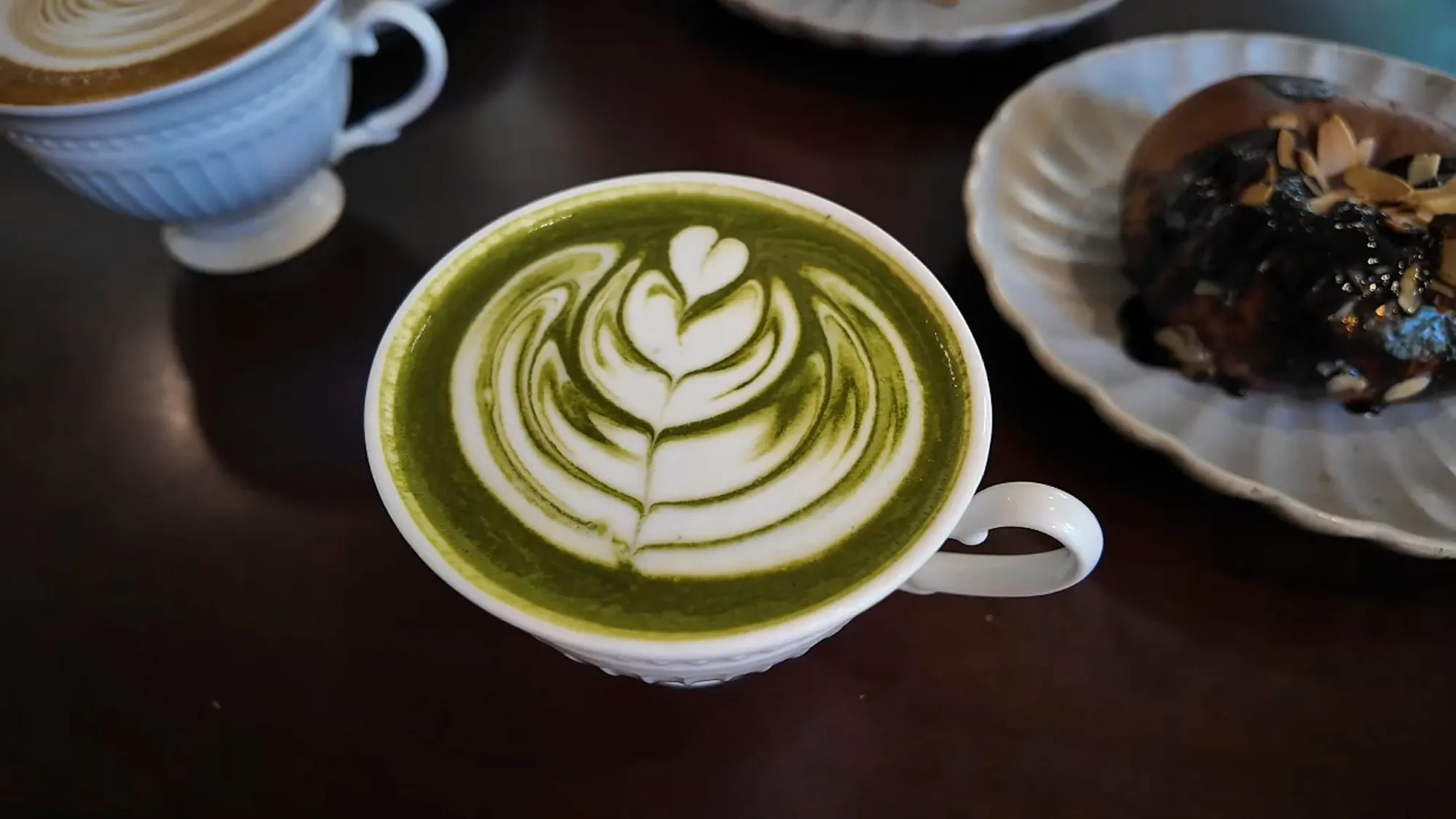 Bright green dirty matcha latte with leaf latte art in a white cup, with the chocolate bagel beside it.