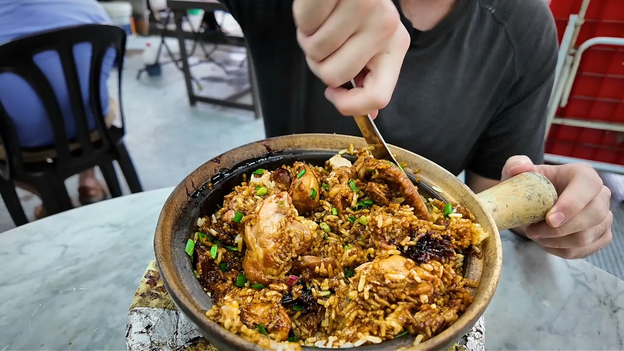 Mixing the steaming claypot chicken rice with chicken and spring onions at the table at 168, Kuala Lumpur.