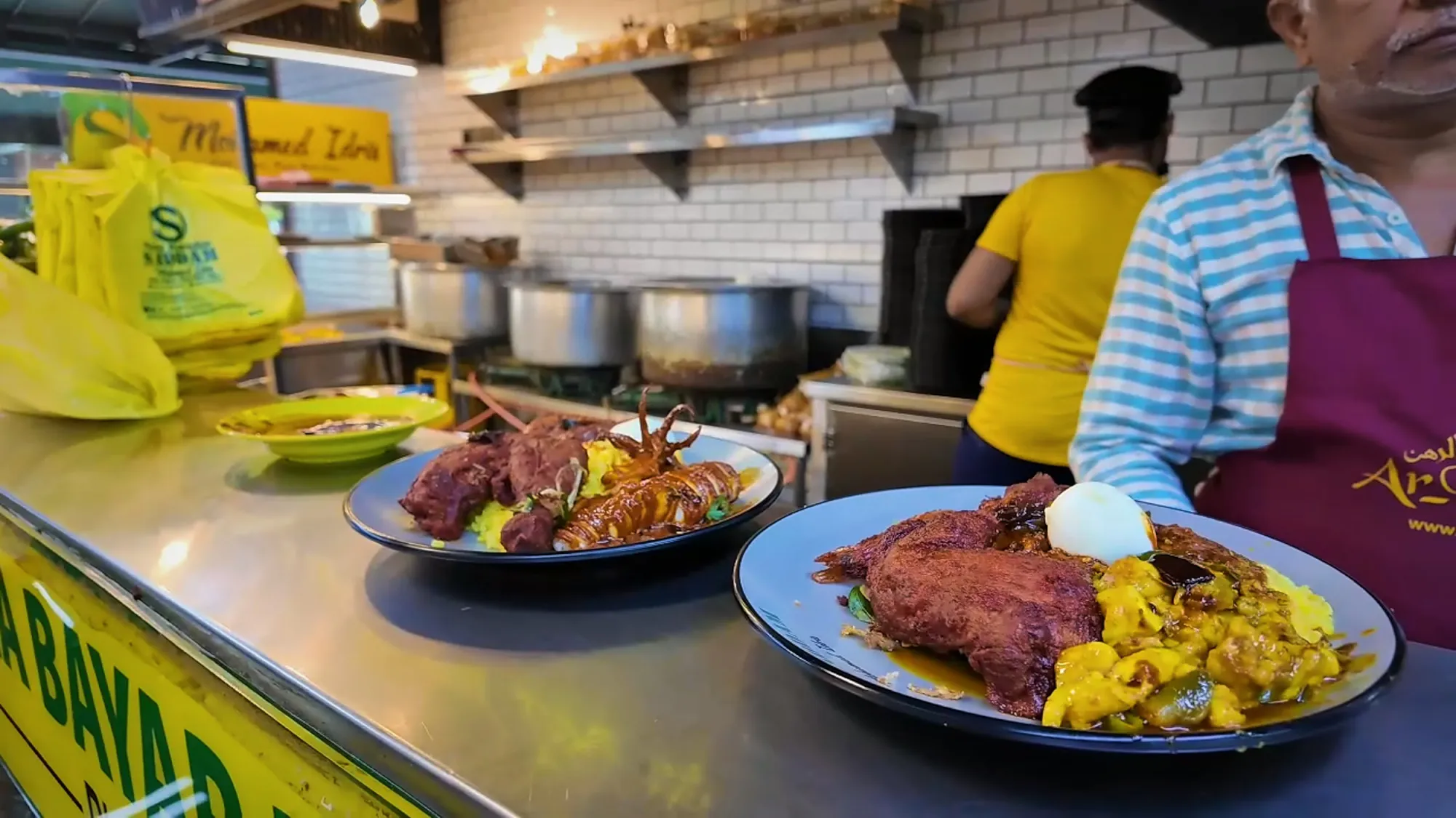 Freshly built plates of nasi kandar with fried chicken, prawns, and curry waiting on the counter at Saddam Nasi Kandar in Kuala Lumpur.