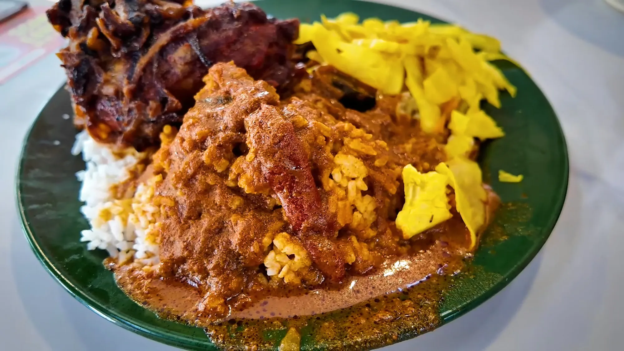 Rice flooded with mixed curry beside onion-covered fried chicken and yellow cabbage on a green plate at Line Clear, Kuala Lumpur.