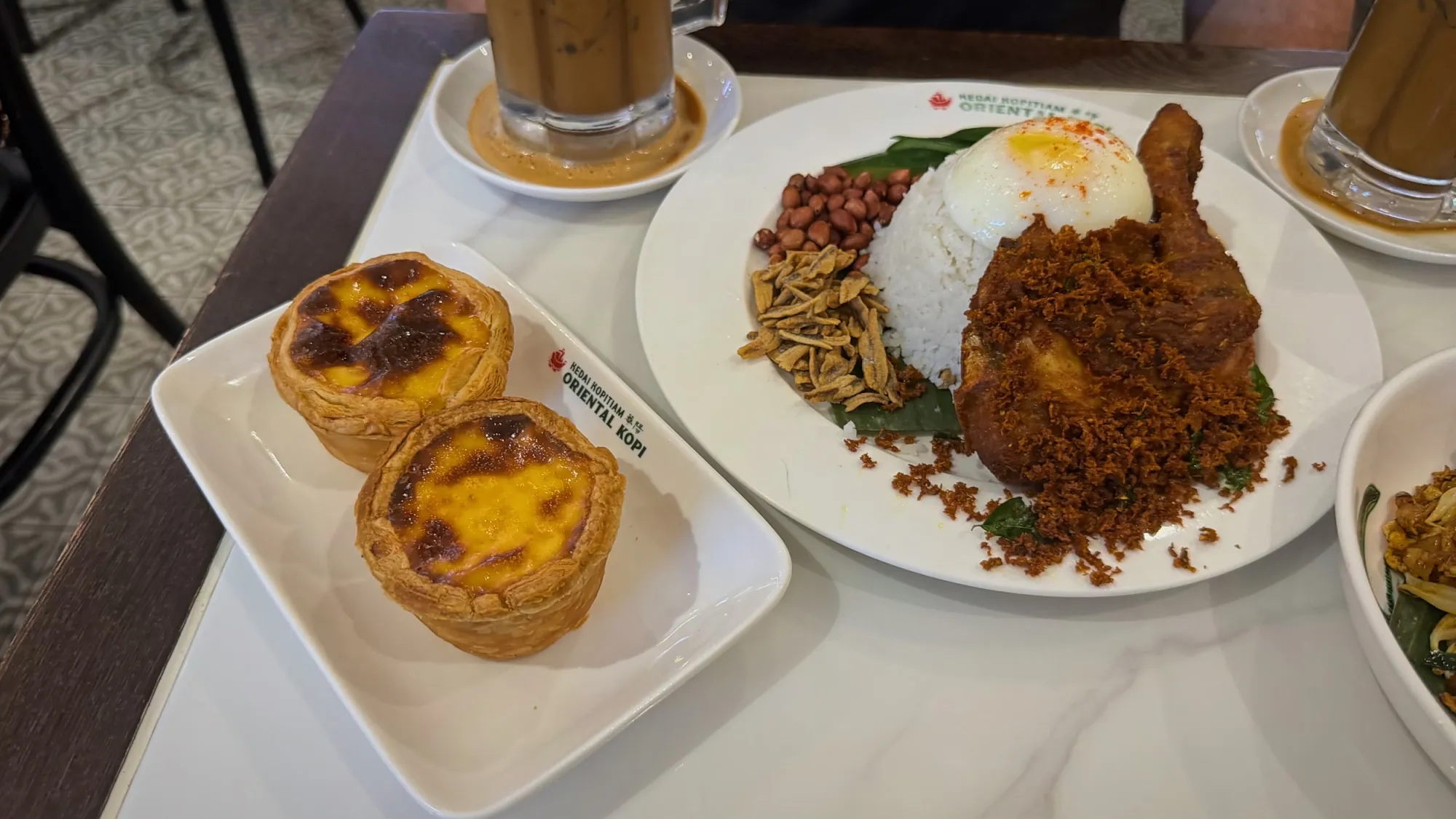 Two Oriental Kopi egg tarts beside a plate of nasi lemak with fried chicken