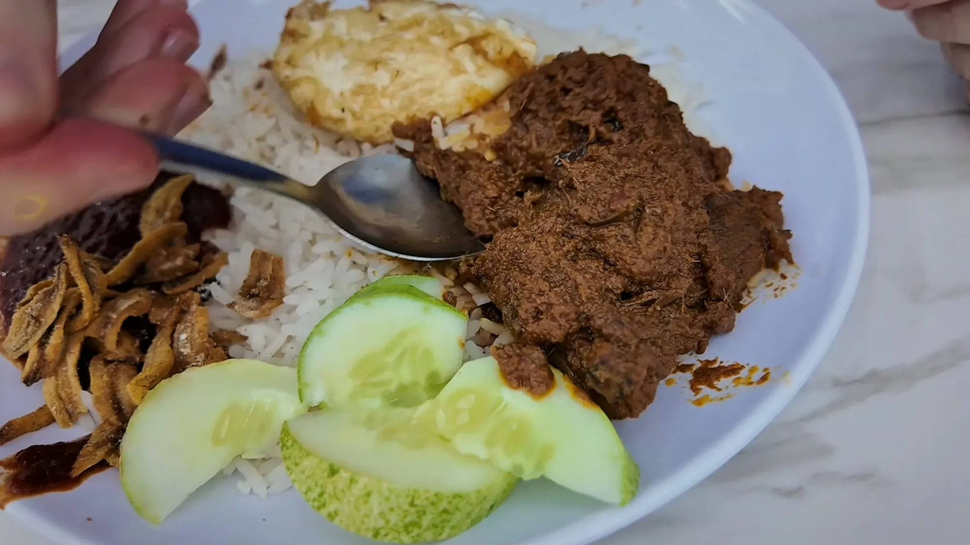 A plate of nasi lemak at Wanjo with dark beef rendang, fried anchovies, cucumber slices, a fried egg, and coconut rice.