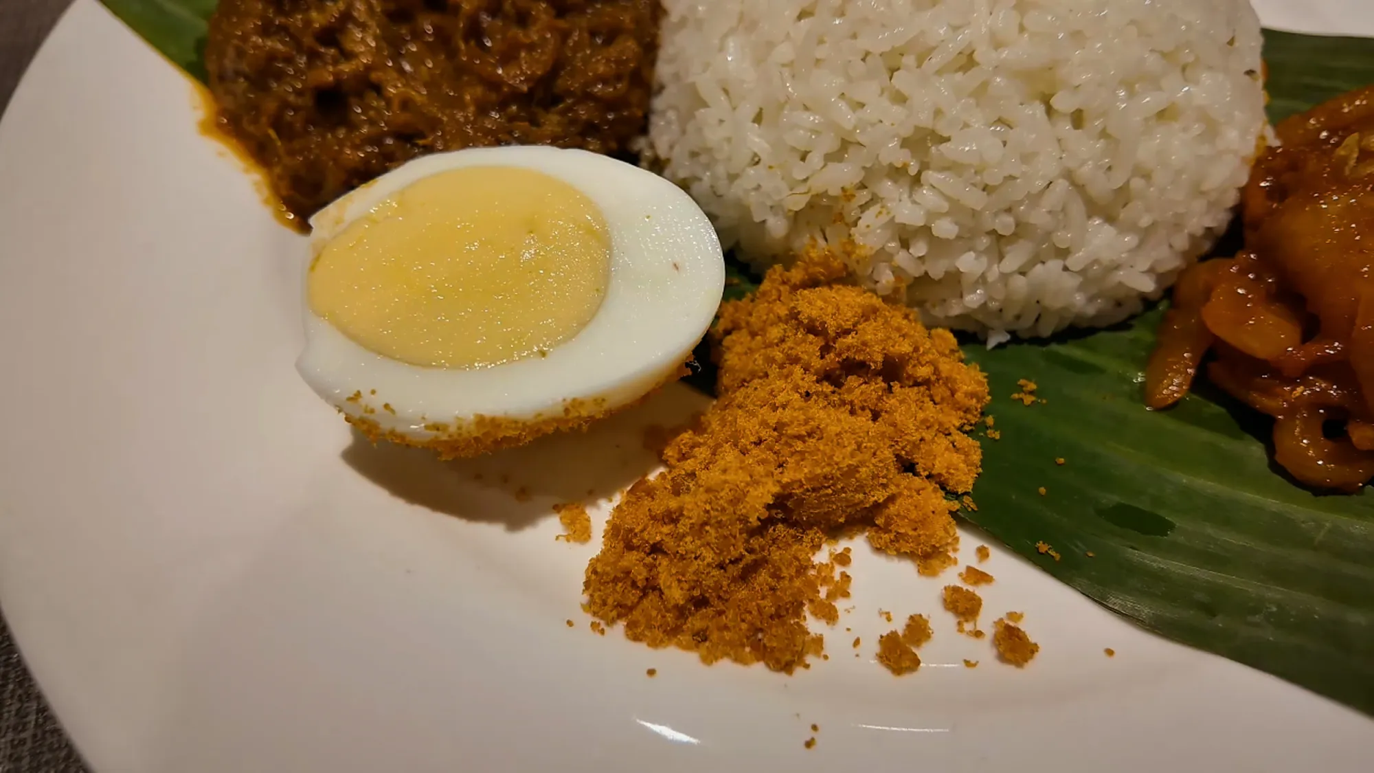 A close-up of Madam Kwan's nasi lemak on a banana leaf with a boiled egg, shrimp floss, coconut rice, and pickled vegetables.