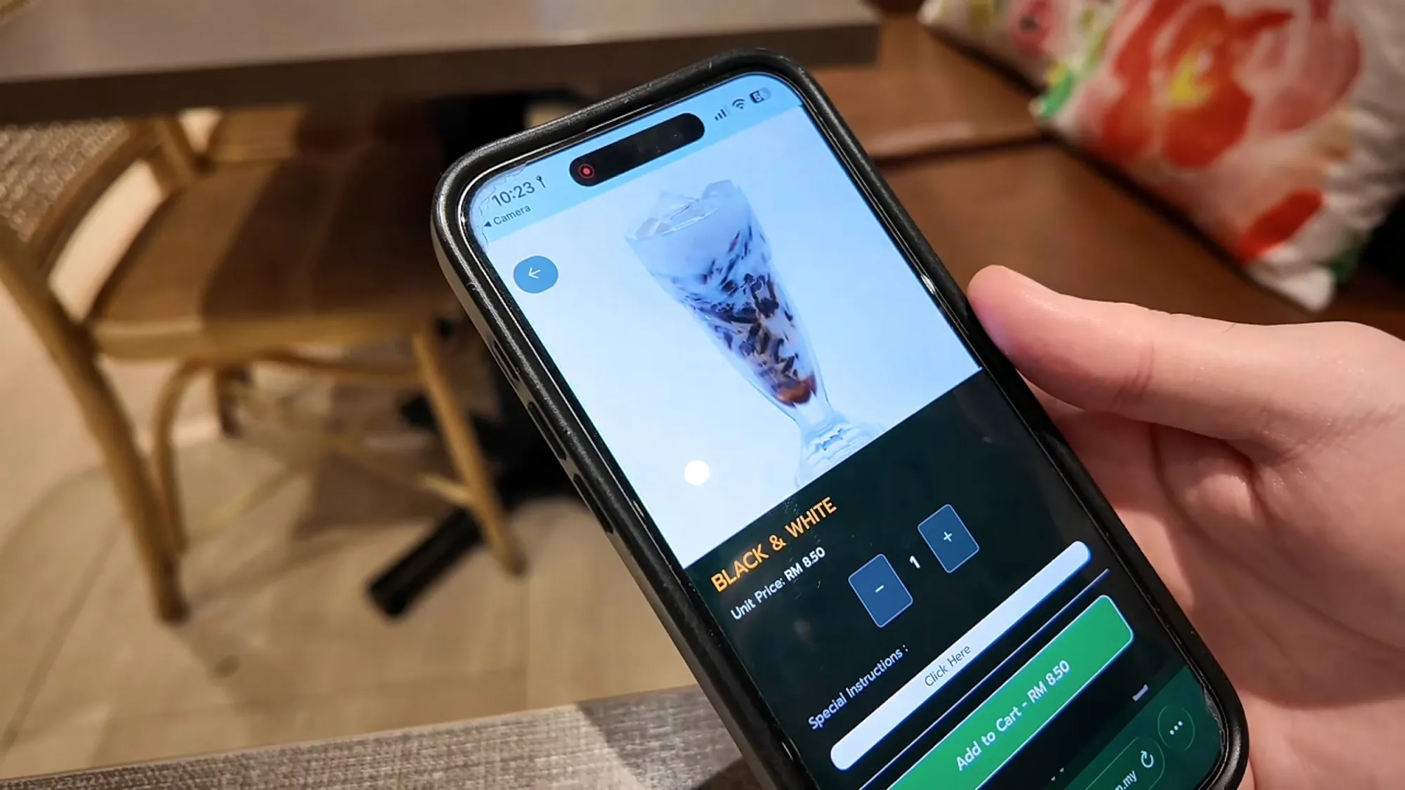 A hand holding a phone with a food and drink ordering app open on the screen in Kuala Lumpur.
