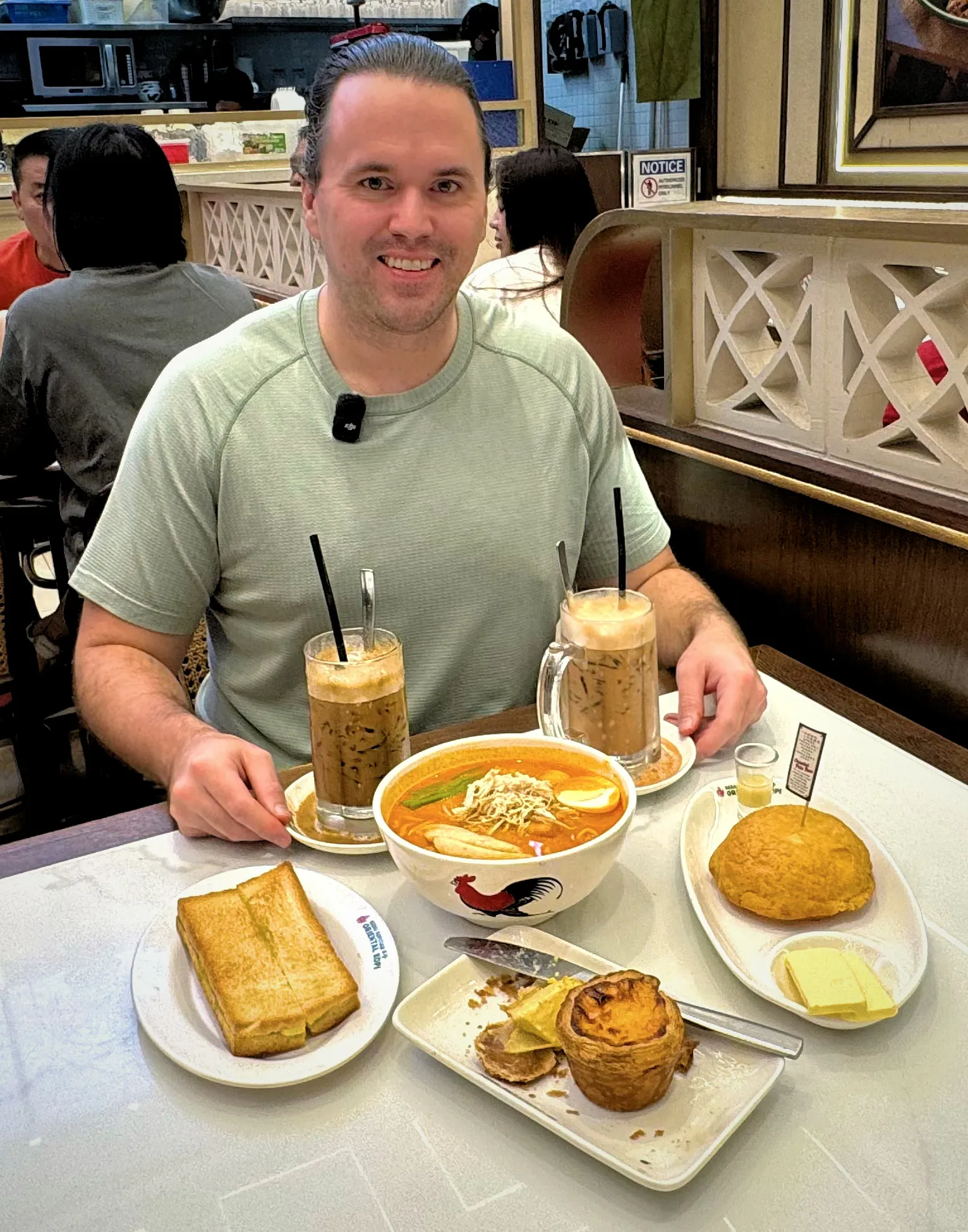 A spread of curry laksa, an egg tart, a polo bun, kaya toast, and iced drinks at Oriental Kopi in Kuala Lumpur