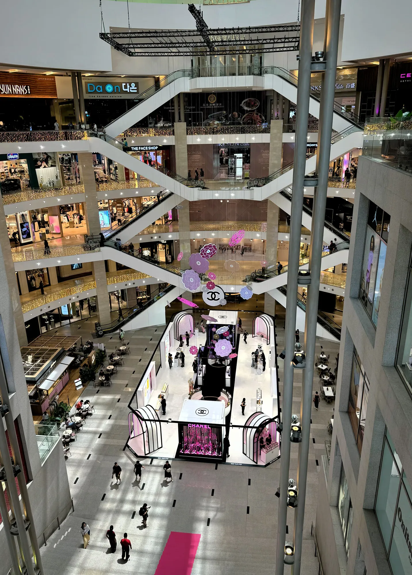 Looking down through the multi-level atrium of Pavilion Kuala Lumpur, with escalators and a pink Chanel exhibition.
