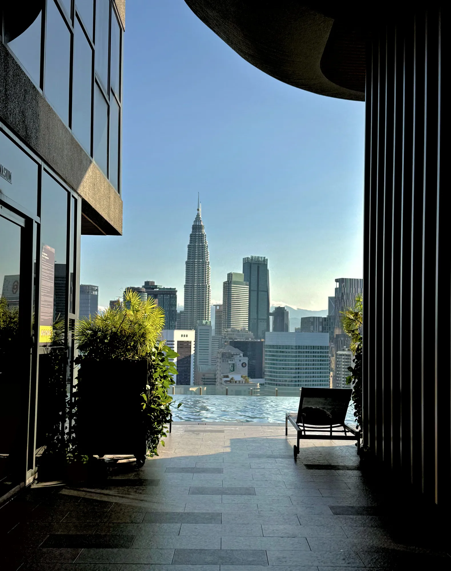 The Petronas Twin Towers in soft morning light, framed by the shaded overhang of a rooftop terrace in Kuala Lumpur.