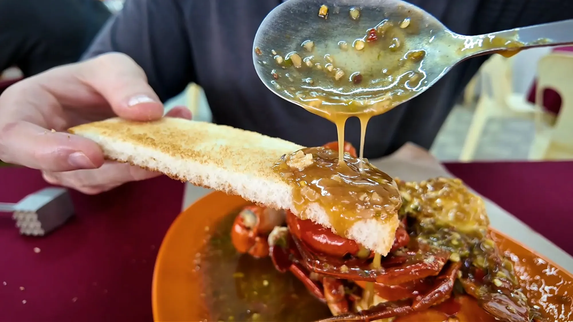 Spooning sweet and sour chilli crab sauce onto a slice of toast over the crab plate at Fatty Crab, Petaling Jaya.