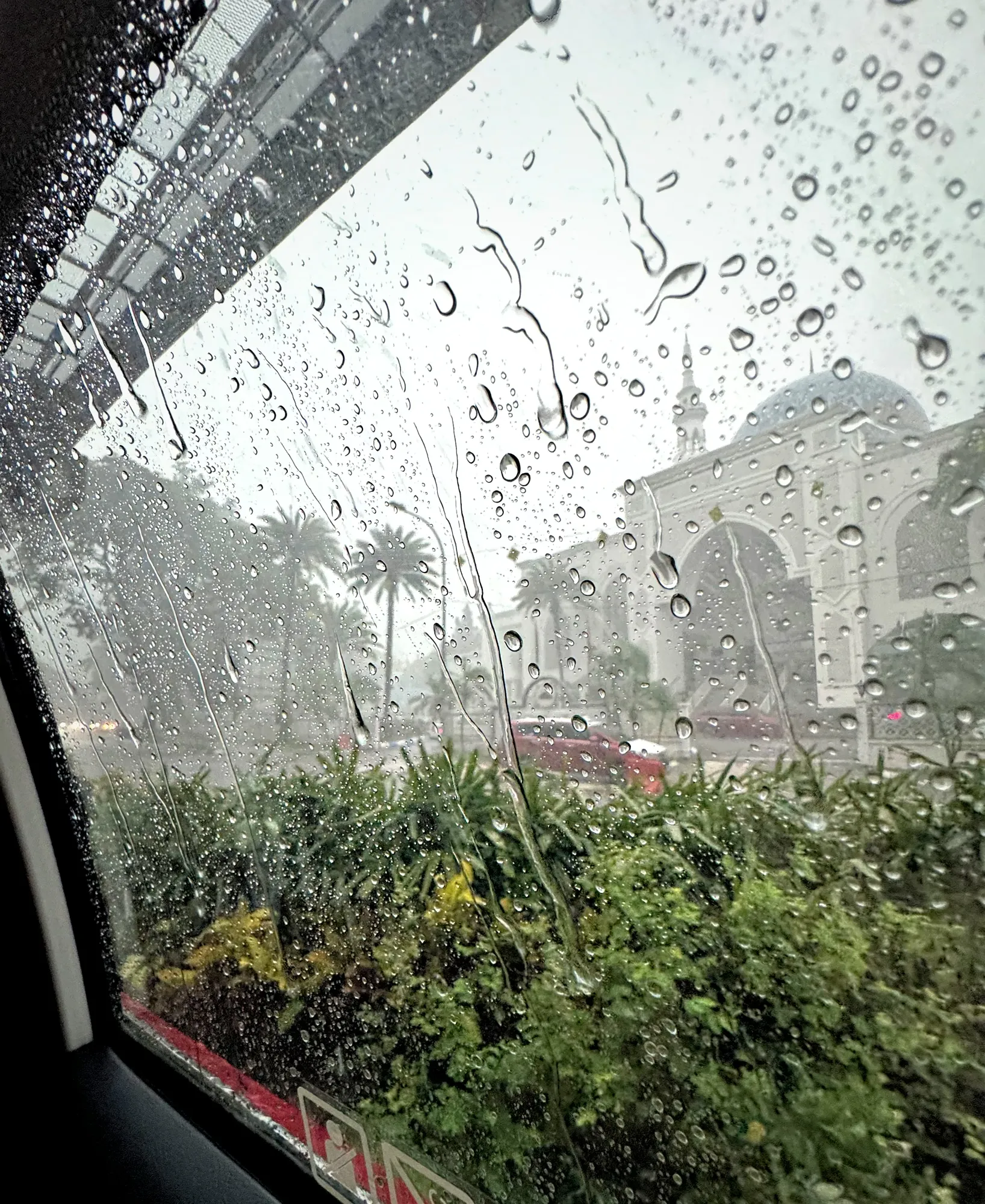 Heavy rain on a car window overlooking palm trees and the domed Masjid Jamek mosque during a downpour in Kuala Lumpur