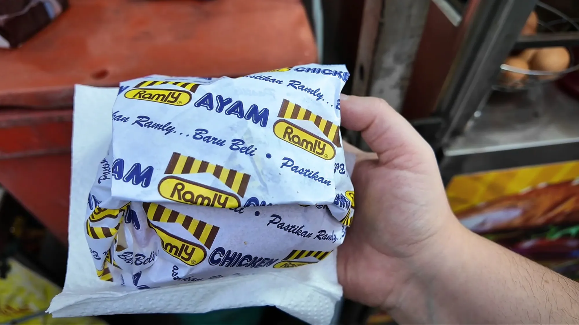 A hand holds a burger in its blue and yellow Ramly wrapper at Boss Burger, Kuala Lumpur