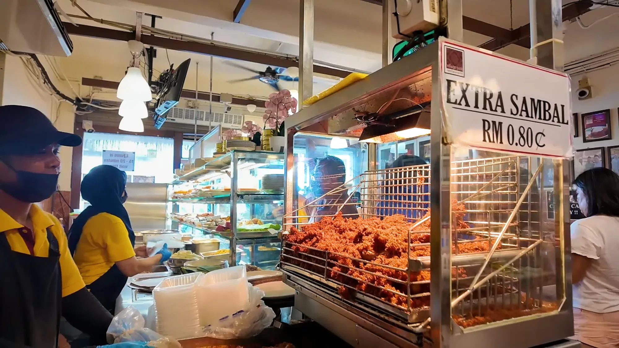 A glass display case filled with crispy fried chicken at a busy Malaysian restaurant counter.
