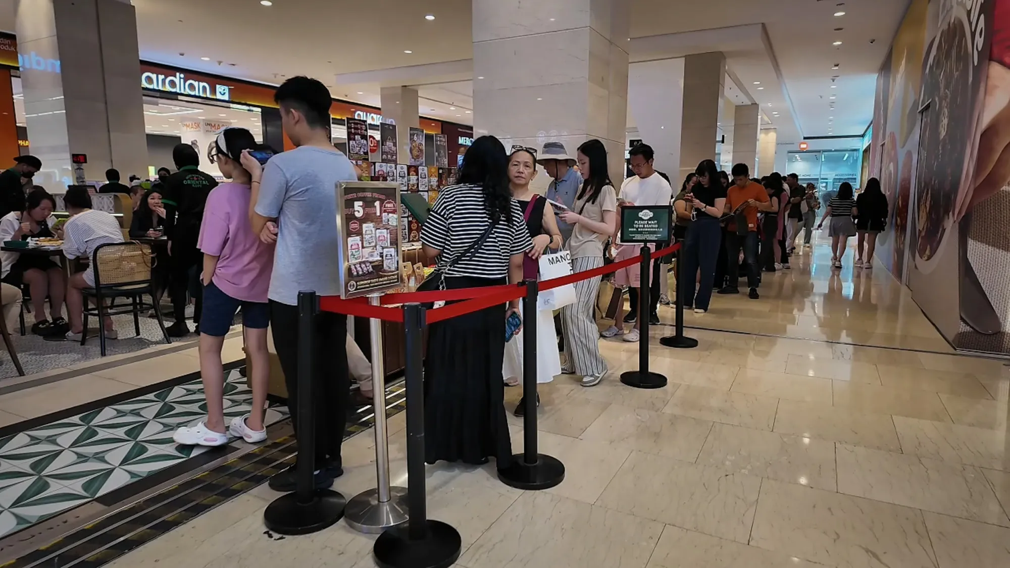 A long queue of people waiting behind red rope barriers outside Oriental Kopi inside Pavilion Kuala Lumpur.