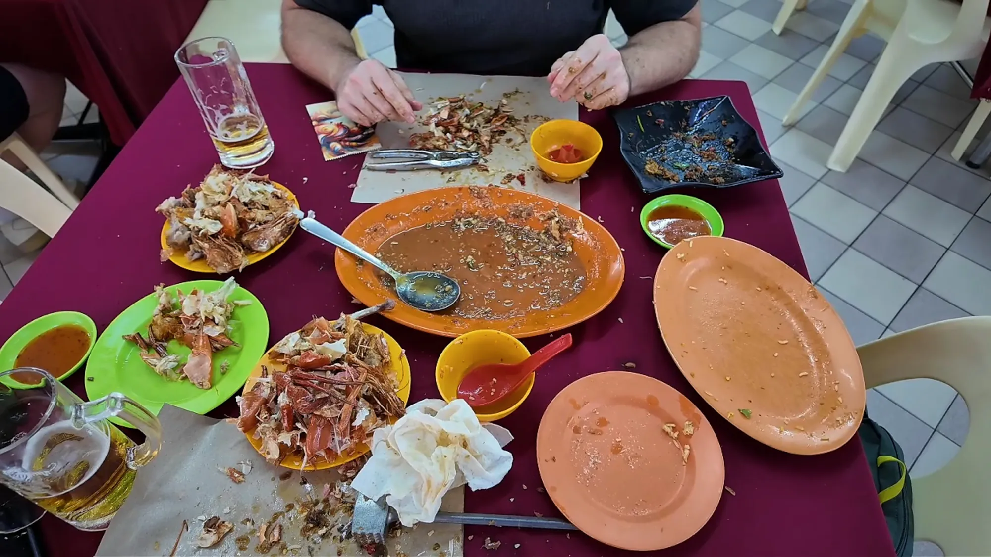 The aftermath of a crab dinner: empty plates, crab shells, used napkins, and sauce on paper sheets at Restoran Fatty Crab.