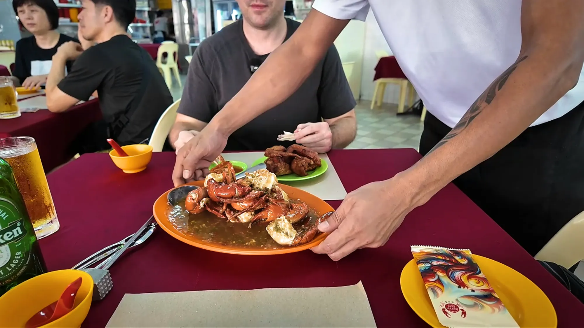 A server setting down a plate of chilli crab on a red tablecloth at Restoran Fatty Crab in Petaling Jaya.